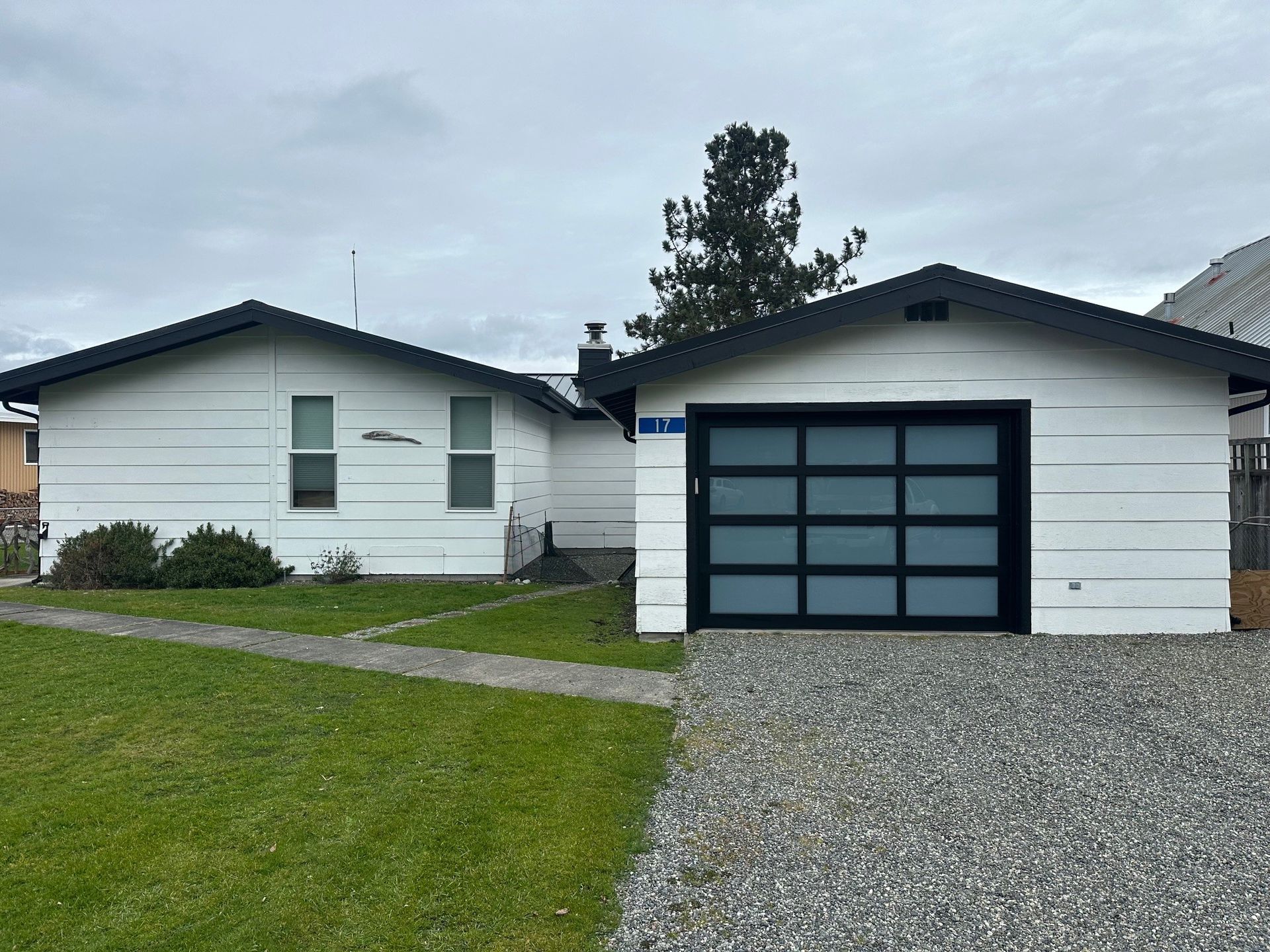 White house with black trim and a garage with a frosted glass door, on a gravel driveway and green lawn.