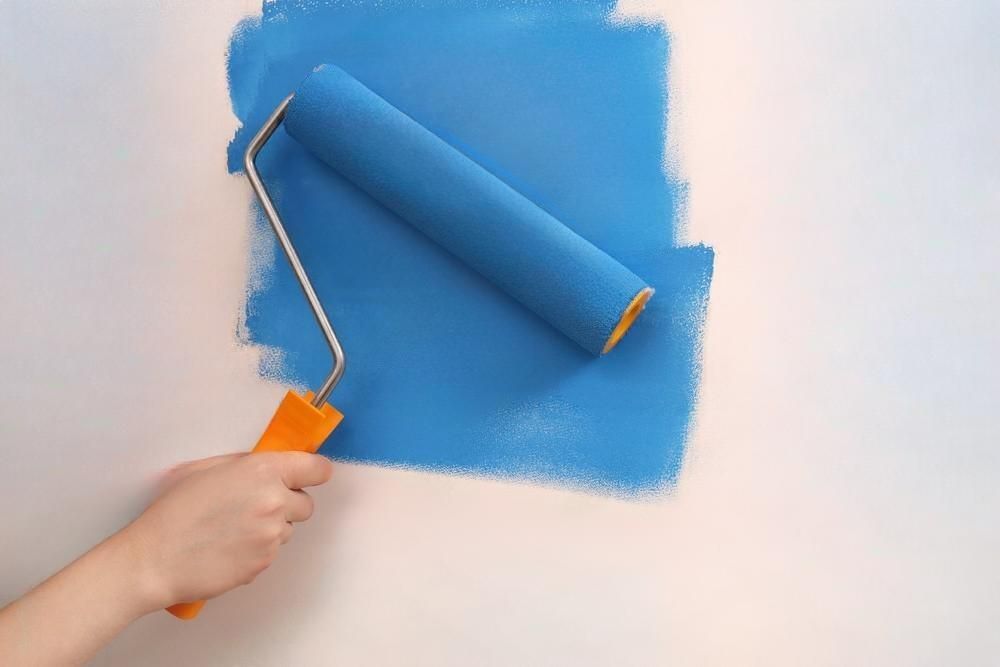 A person is painting a wall blue with a paint roller