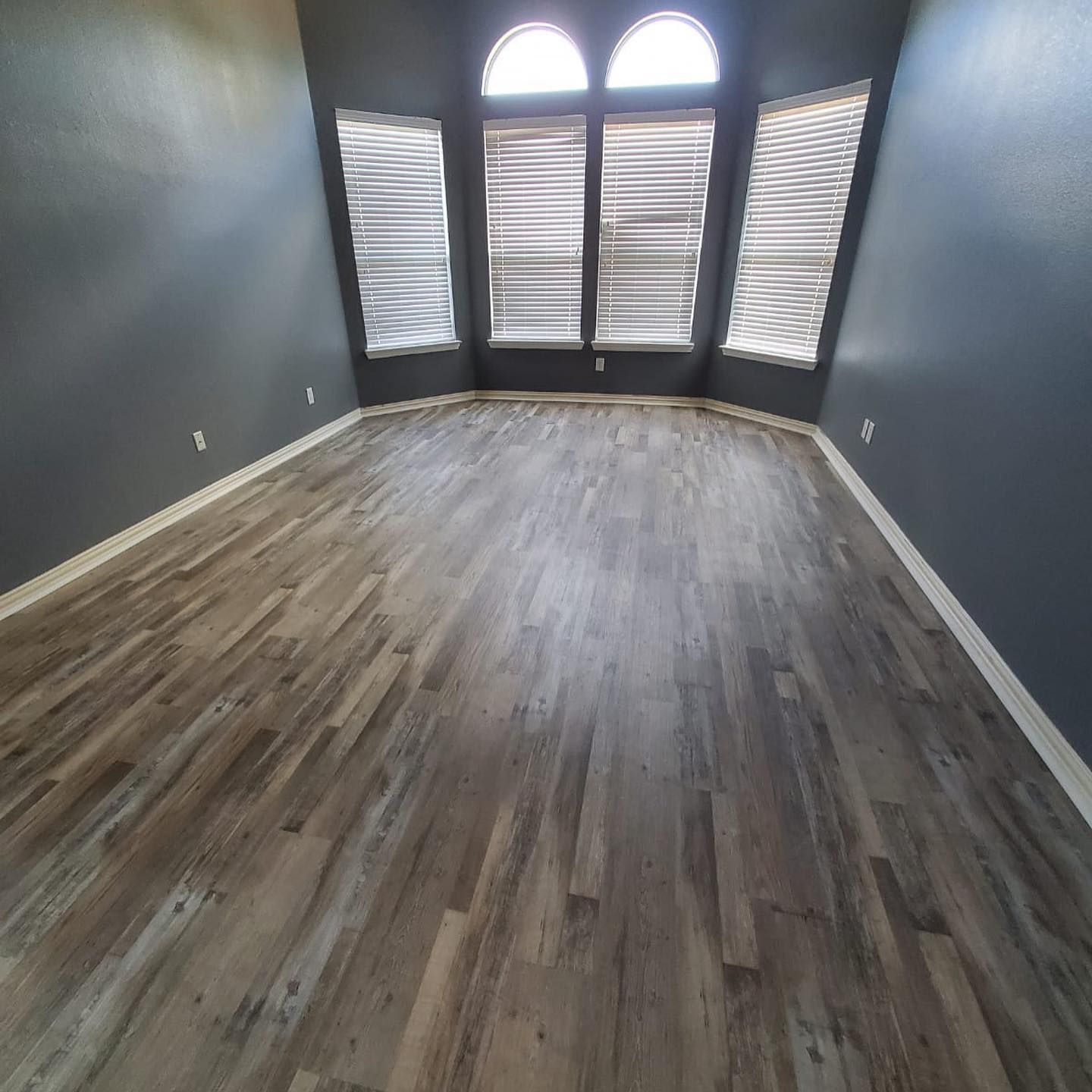 Empty room with gray walls, wood-look flooring, and a curved window with blinds.
