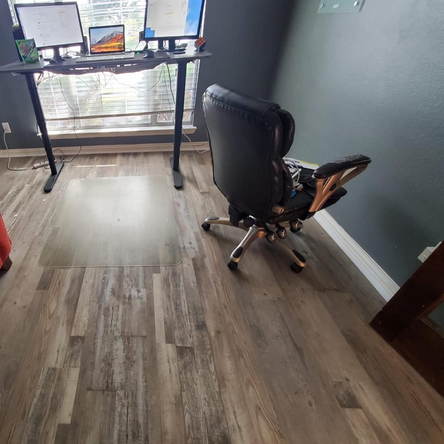 A workspace with a black standing desk, chair, and monitors next to a window.