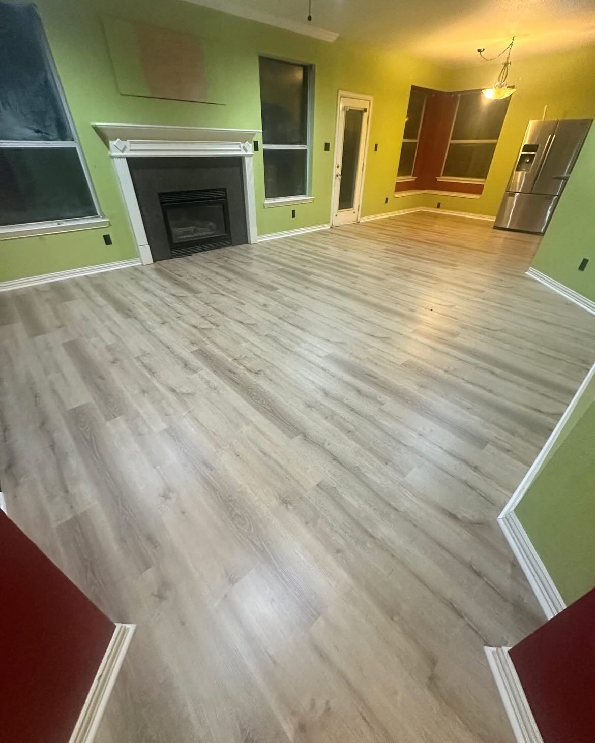 Living room with light wood-look flooring, green walls, fireplace, and stainless steel refrigerator.