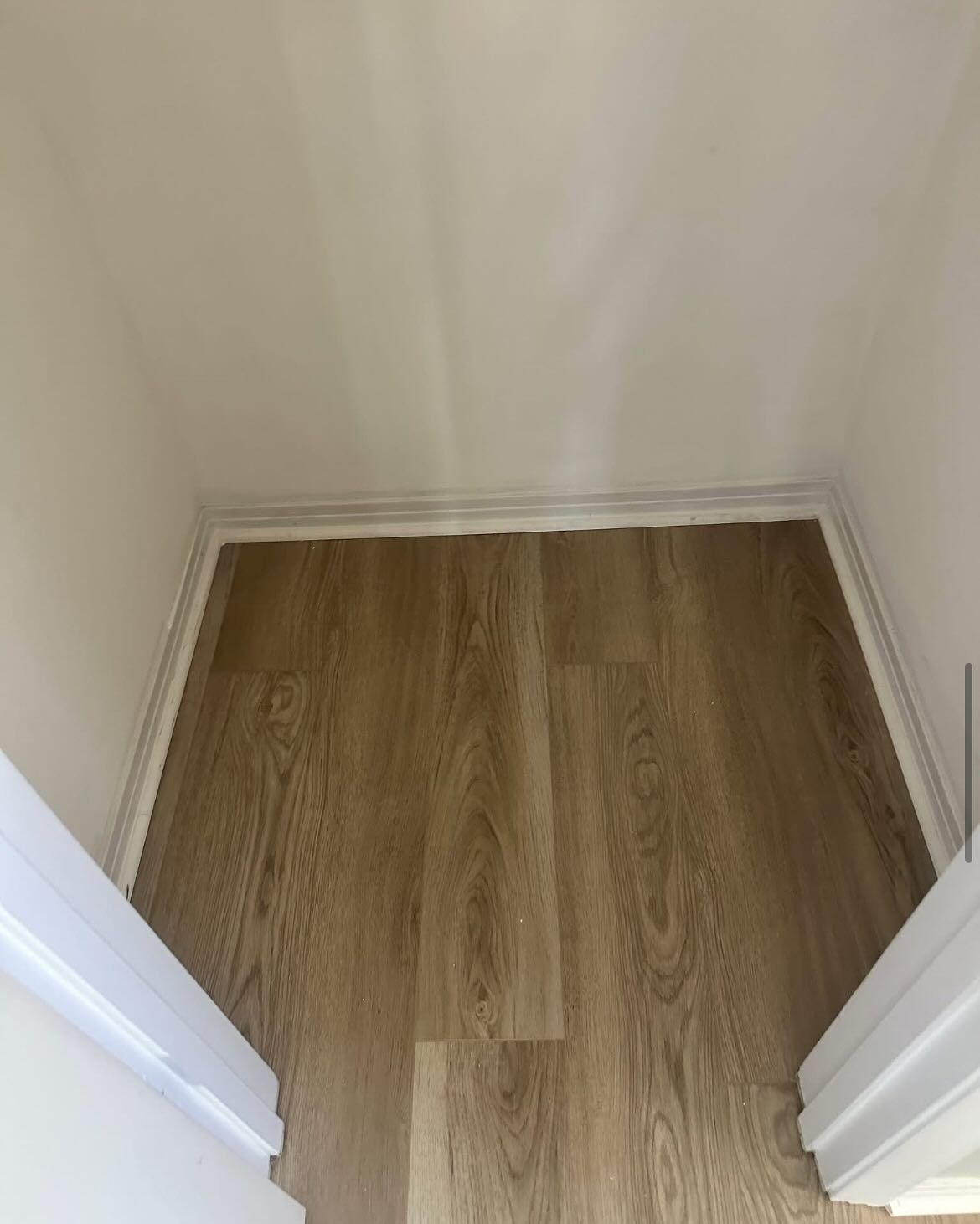 Beige-toned wood-look flooring in a hallway or alcove, framed by white trim and walls.
