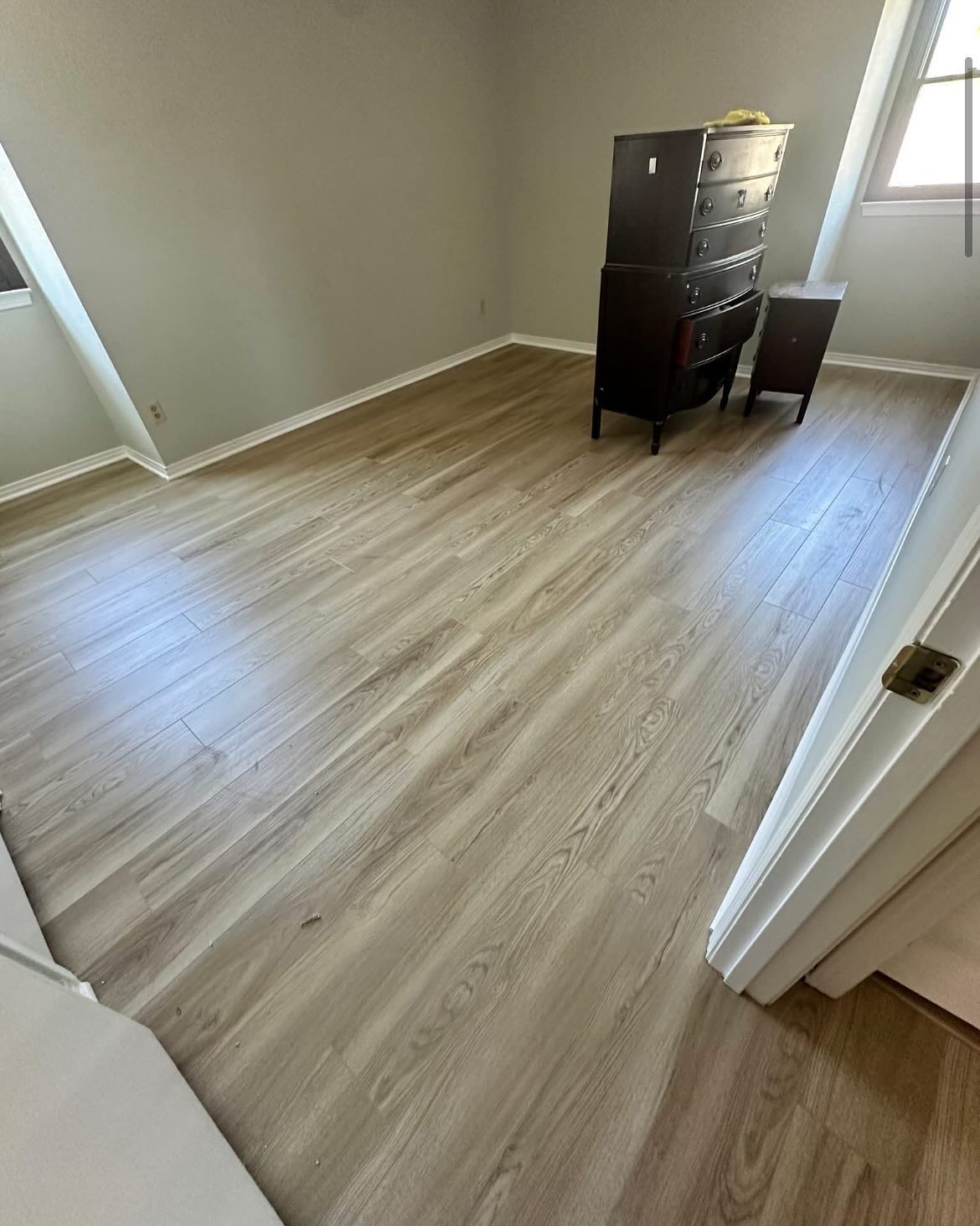 Bedroom with light wood-look flooring, dark dresser and chair. Natural light through a window.