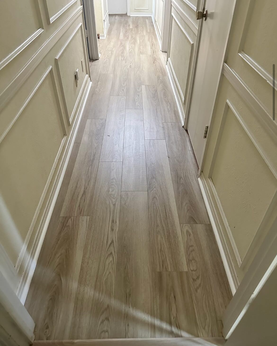 Narrow hallway with light wood-look flooring, white trim, and beige walls.