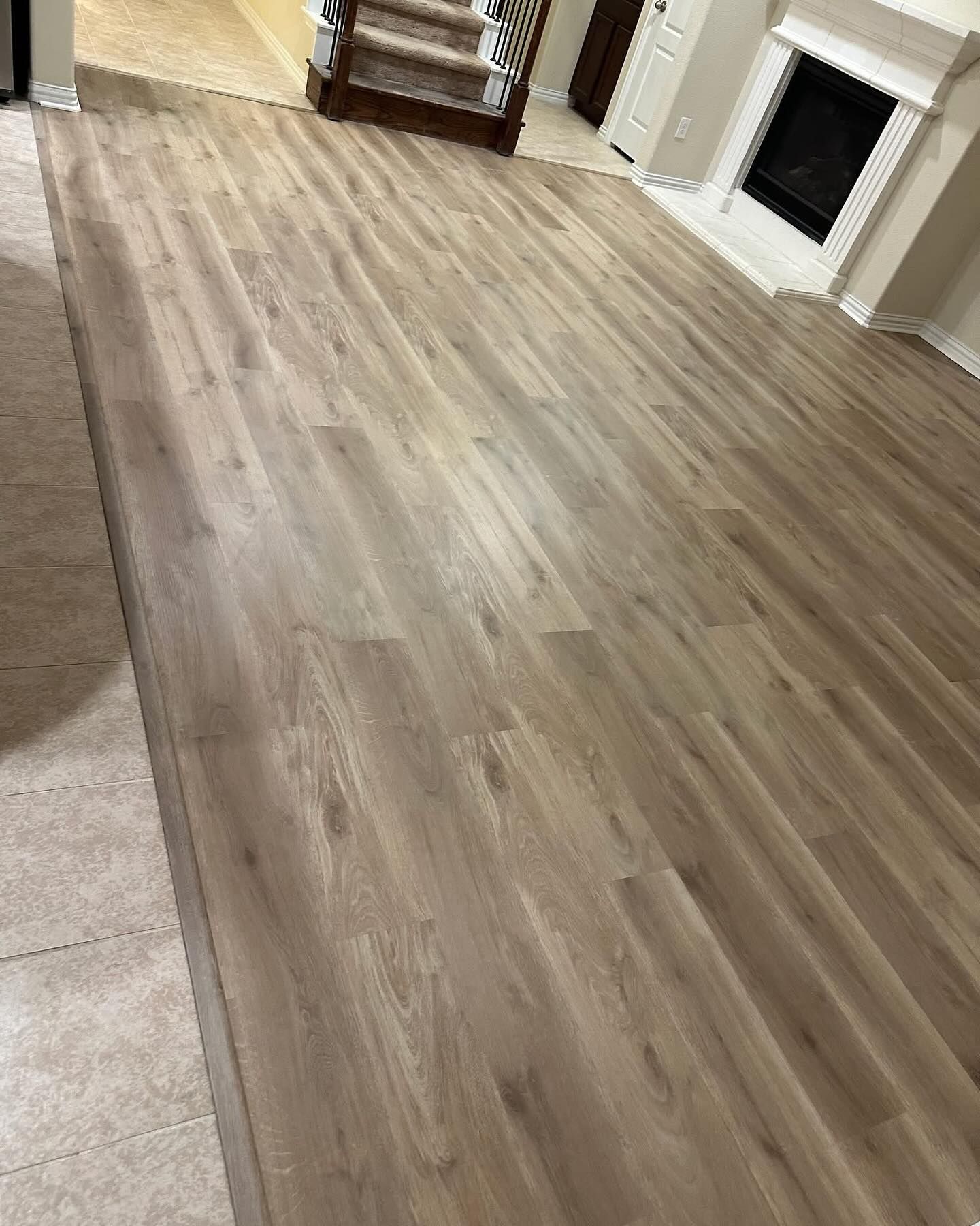 Light brown wood-look flooring in a room, near a fireplace and stairs.
