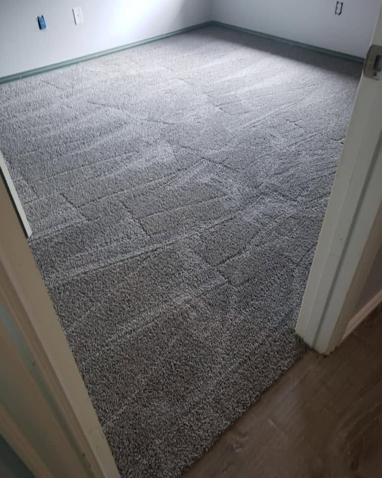 Gray carpeted room, viewed from a doorway. The carpet is installed throughout the room, along the walls.