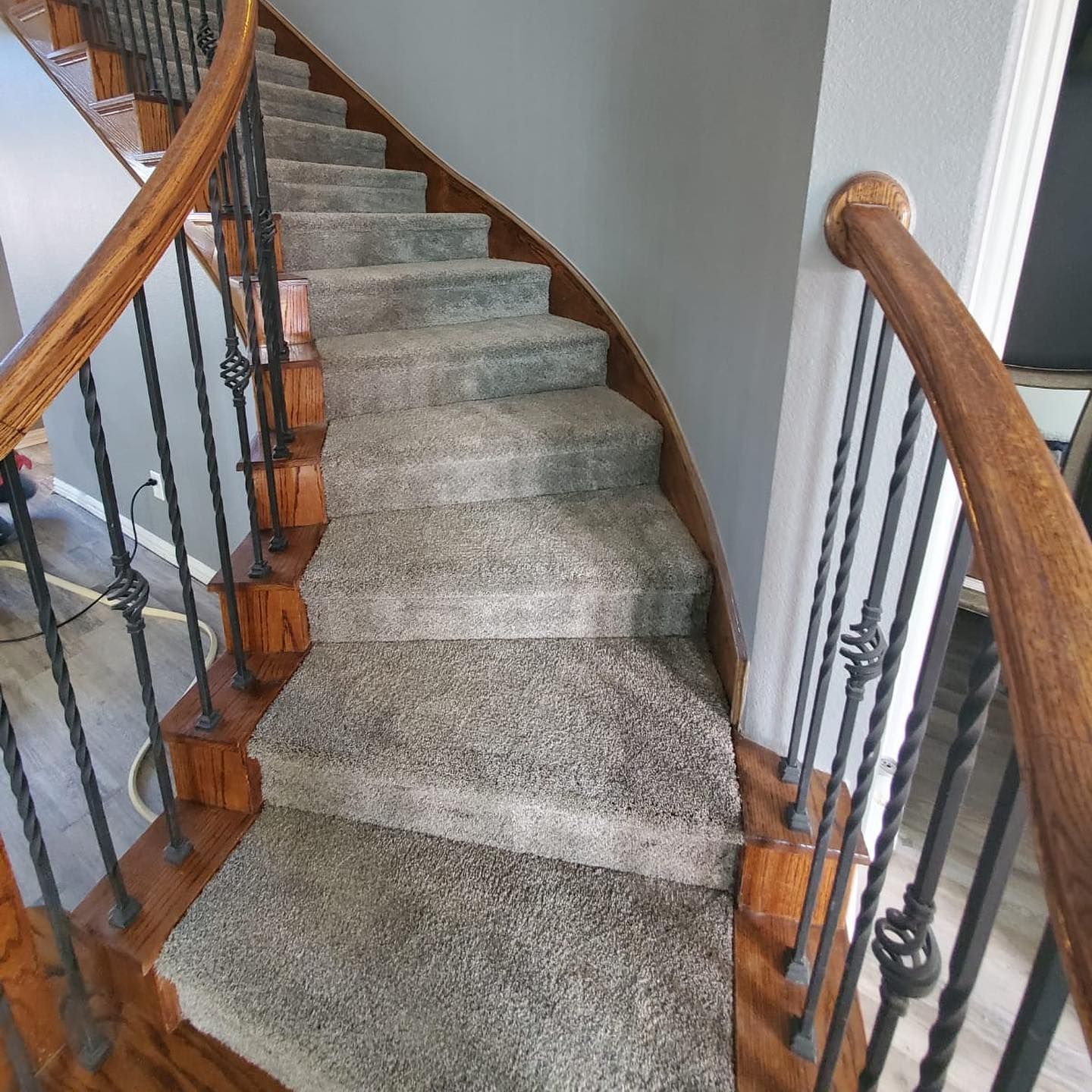 Curved staircase with brown wood handrails and gray carpeted steps. Black iron balusters.