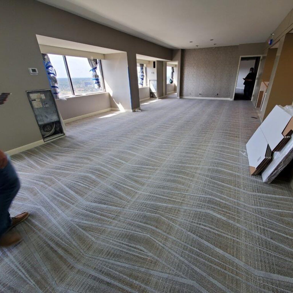 Large empty room with new patterned carpet, windows, and a person standing in the doorway.