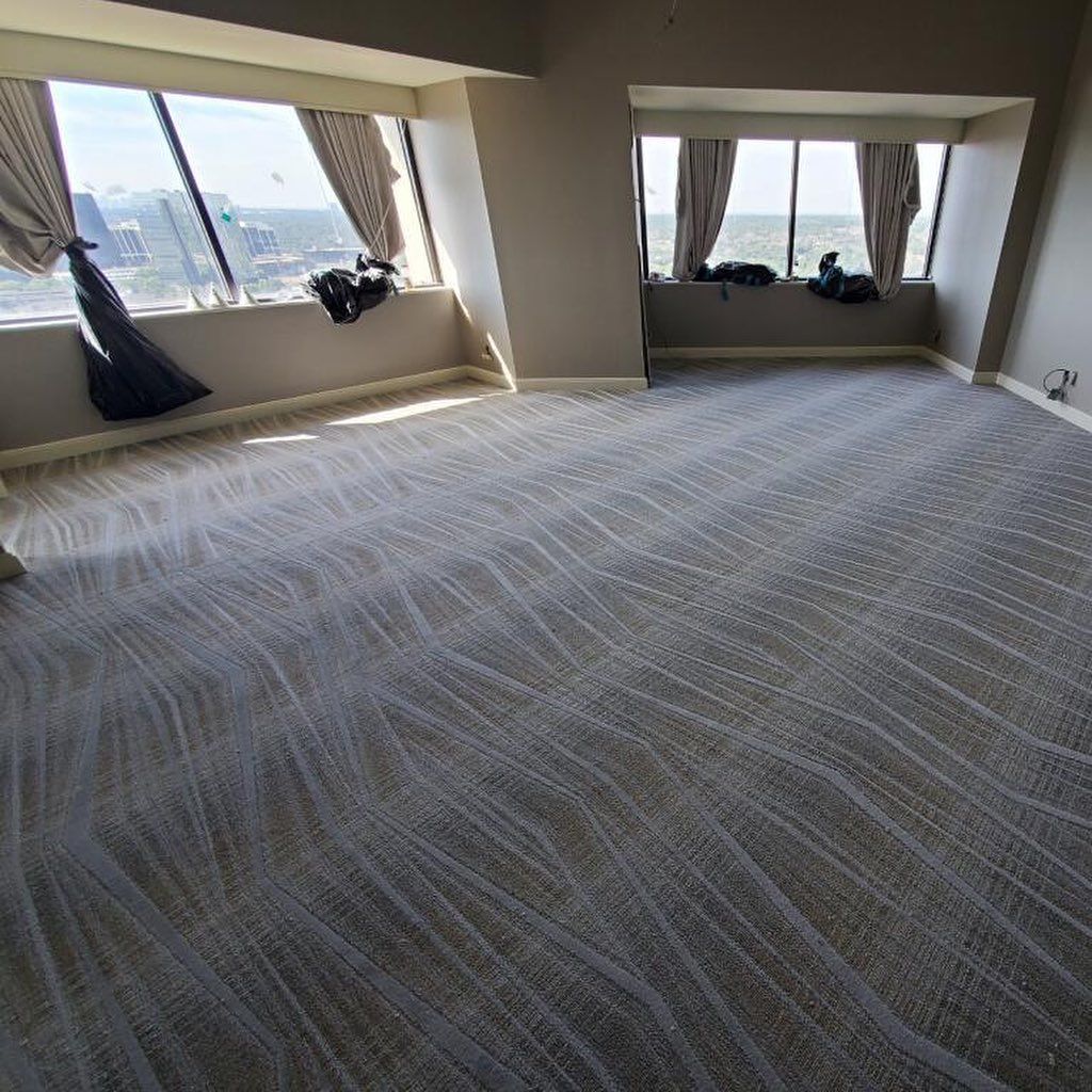 Empty room with patterned gray carpet, large windows, and draped curtains.