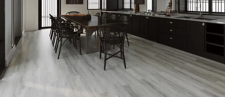 A modern kitchen with black cabinets, dining table, and light wood-look flooring.