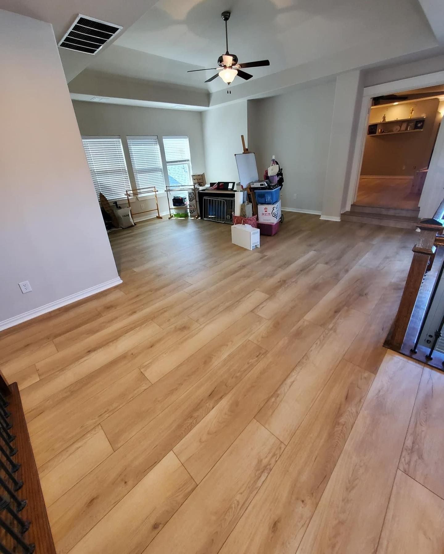 Light-colored wood flooring in a living area. Gray walls, ceiling fan, and sunlight through blinds are visible.