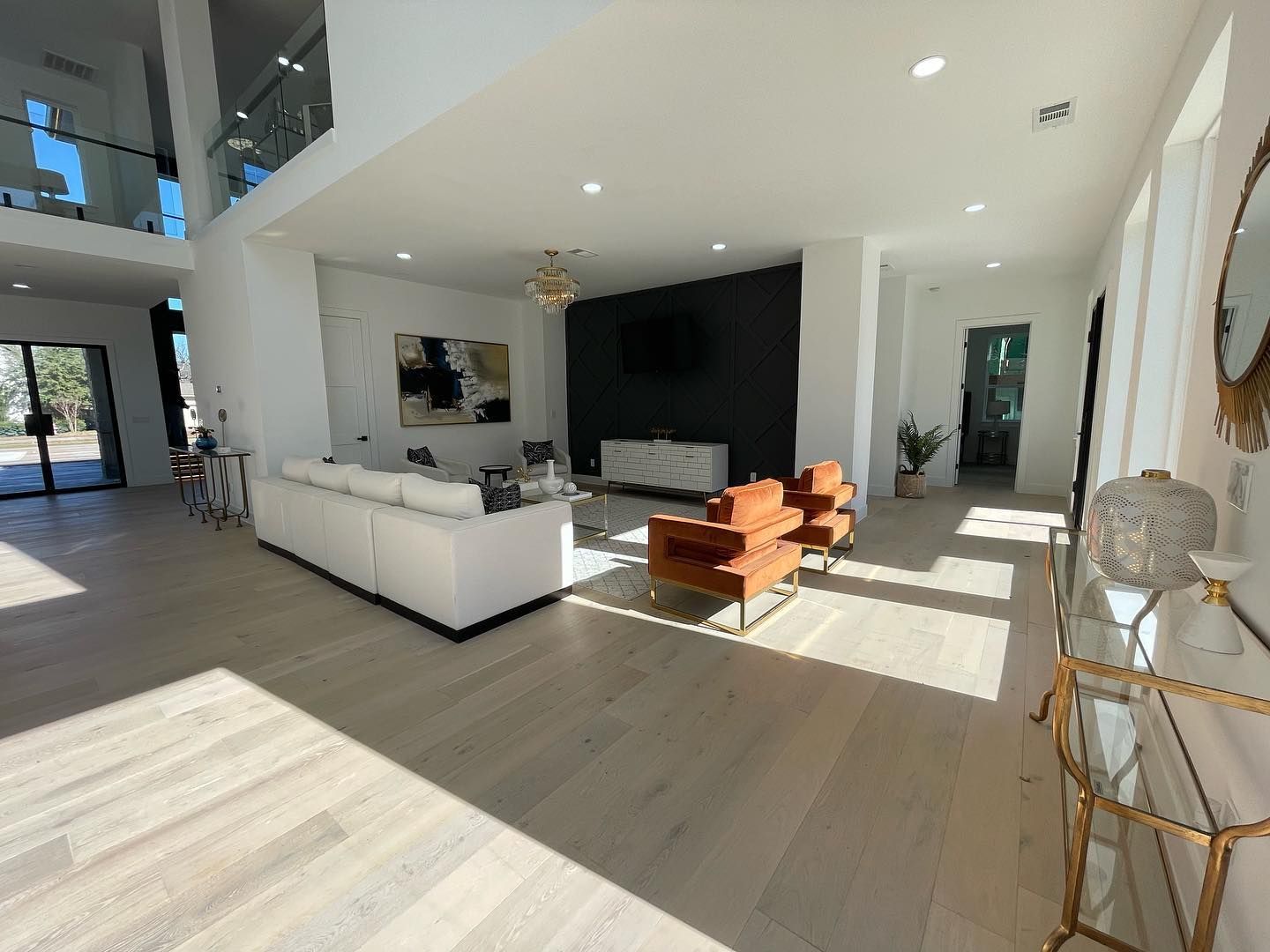 Spacious modern living room with white walls, light wood floors, and orange velvet chairs.