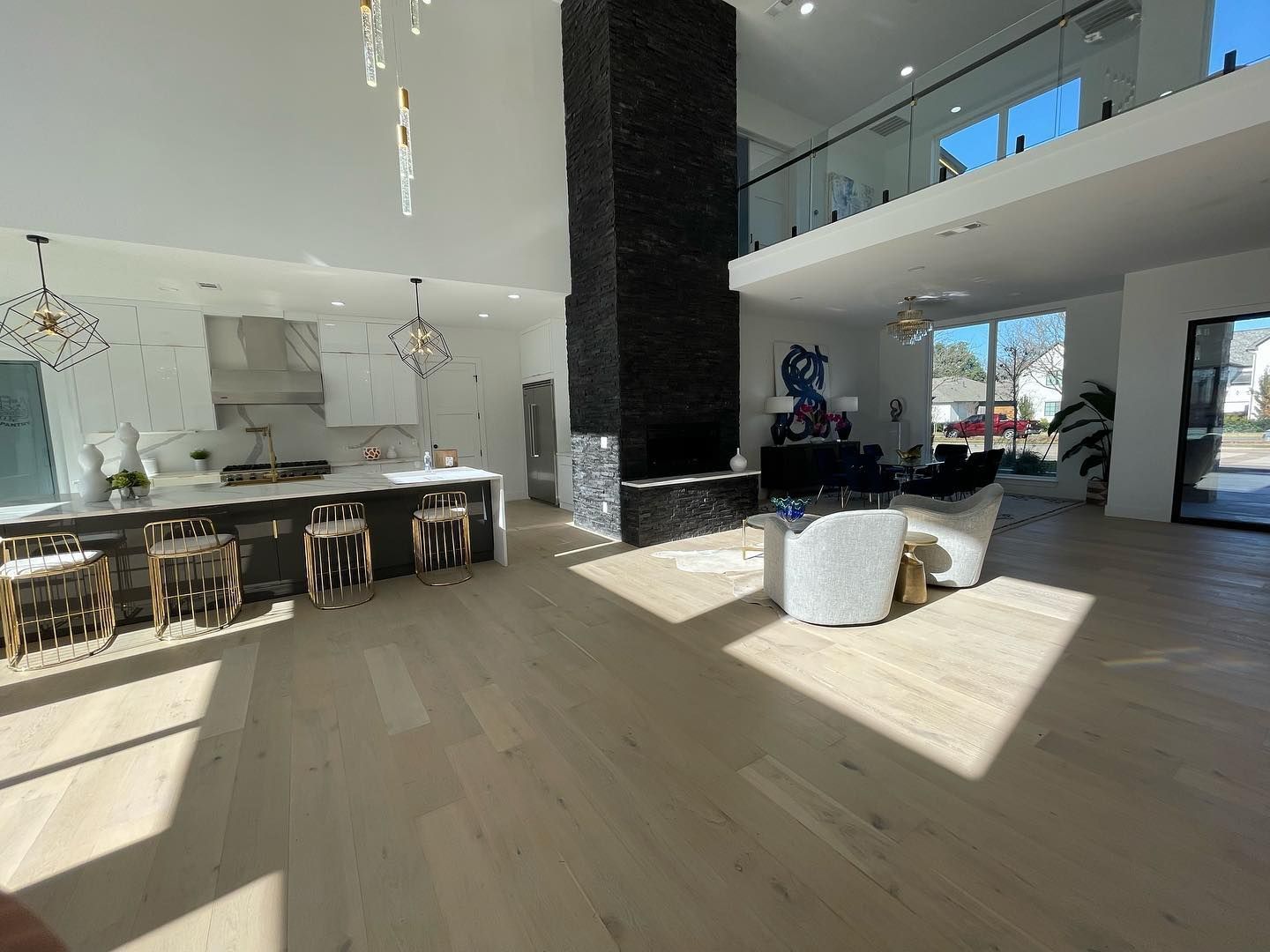 Spacious modern home interior with kitchen, living area, tall black fireplace, and light wood floors.
