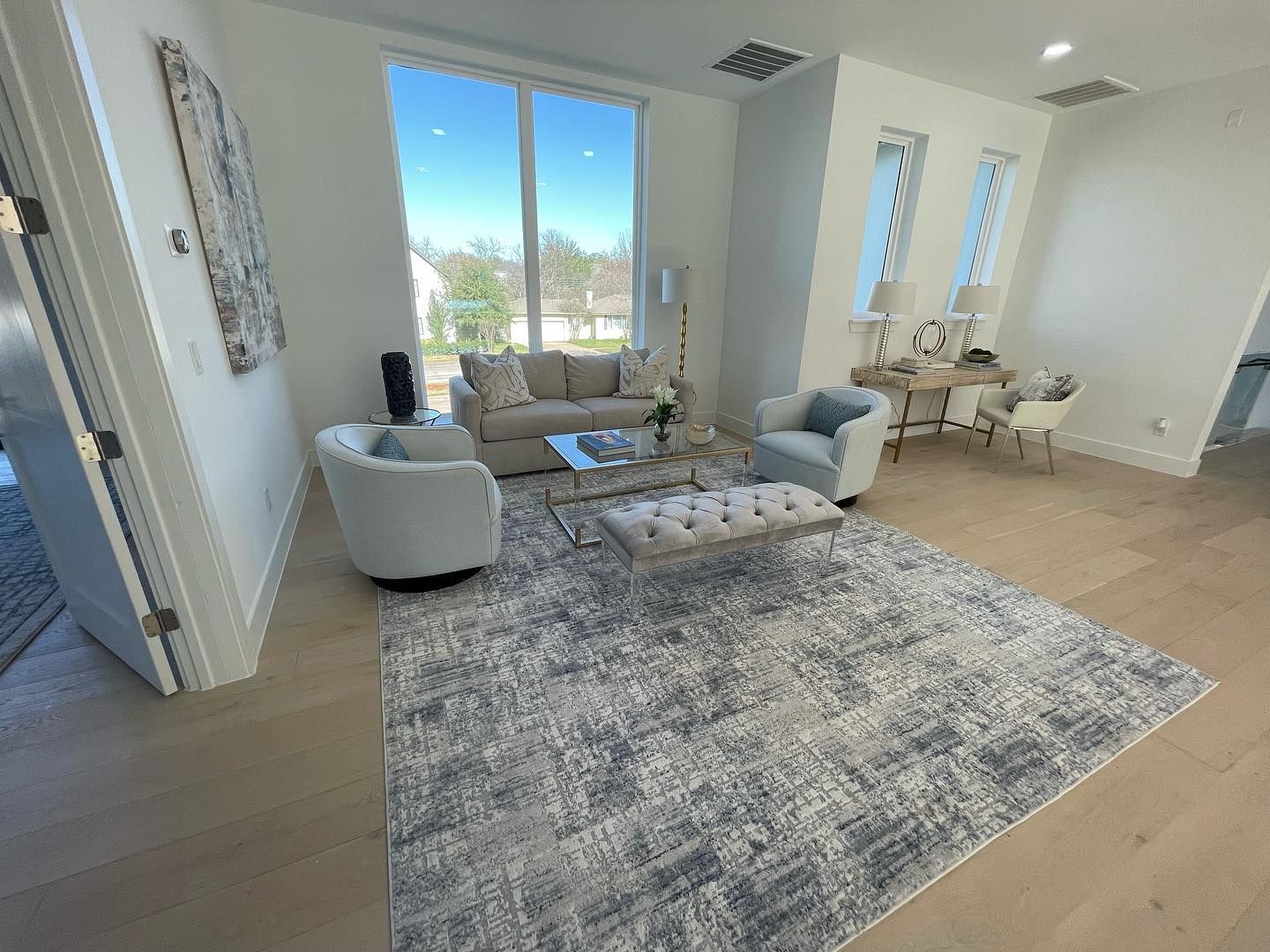 Bright living room with neutral colors, large windows, seating area, and desk.