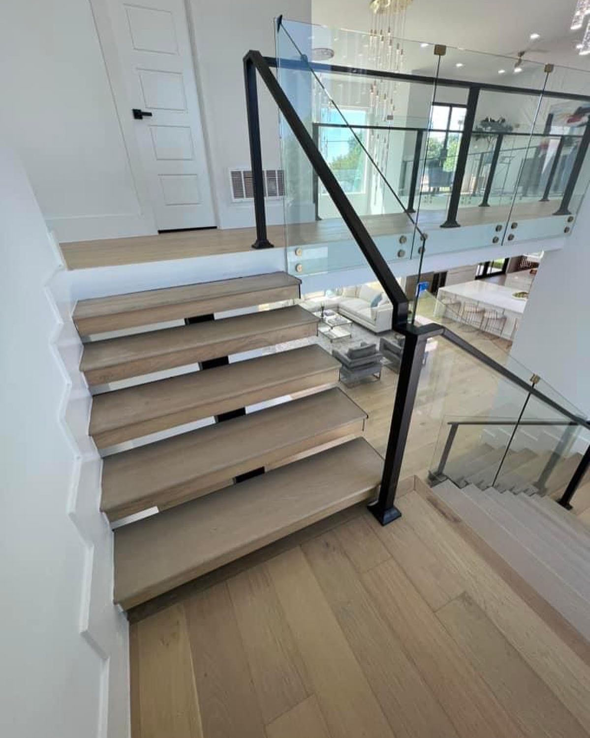 Modern staircase with glass railing and light wood steps, leading to a second-floor landing.