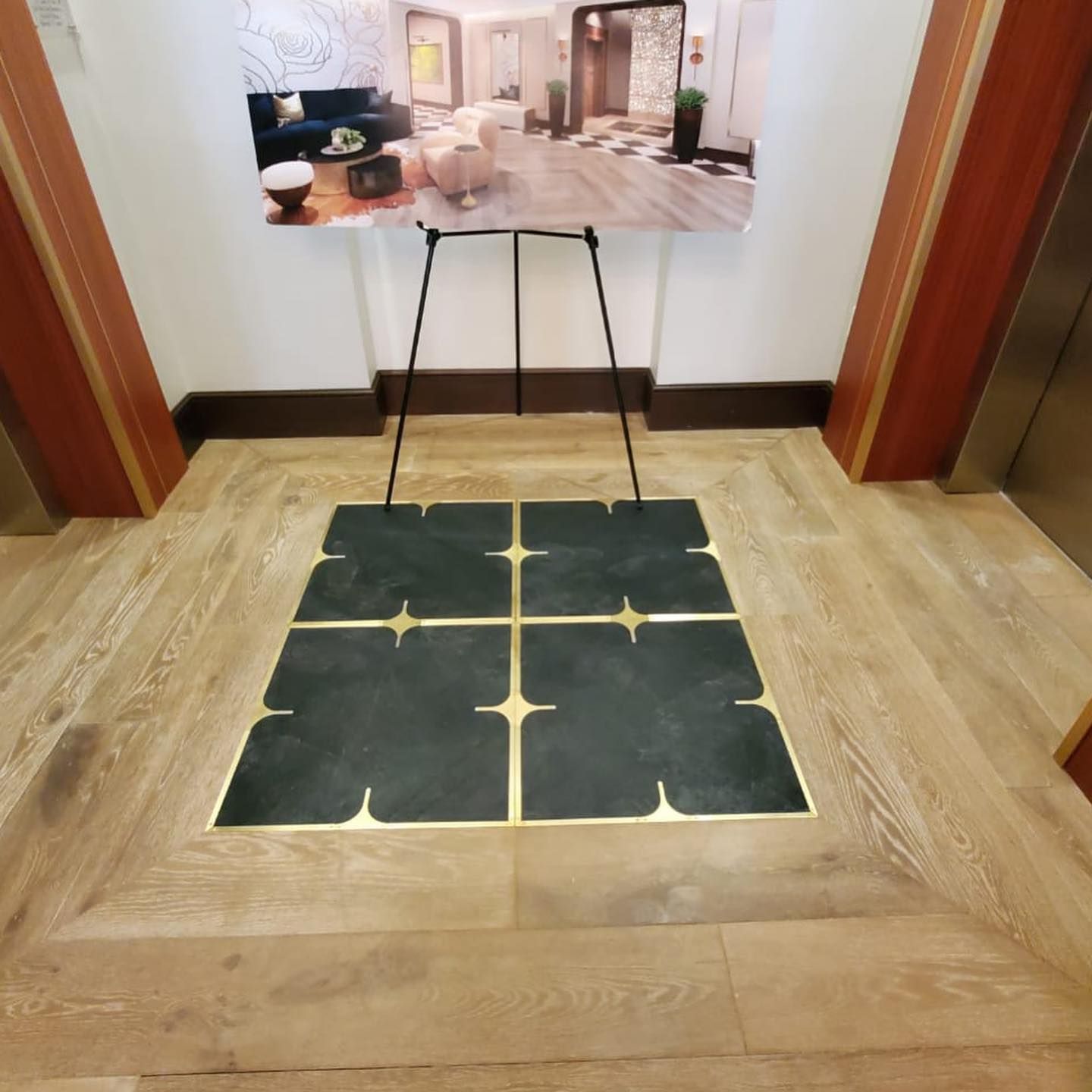 Elevator lobby with wood floor. Display stand holds a photo of the interior. Gold trim and dark tiles accent floor.