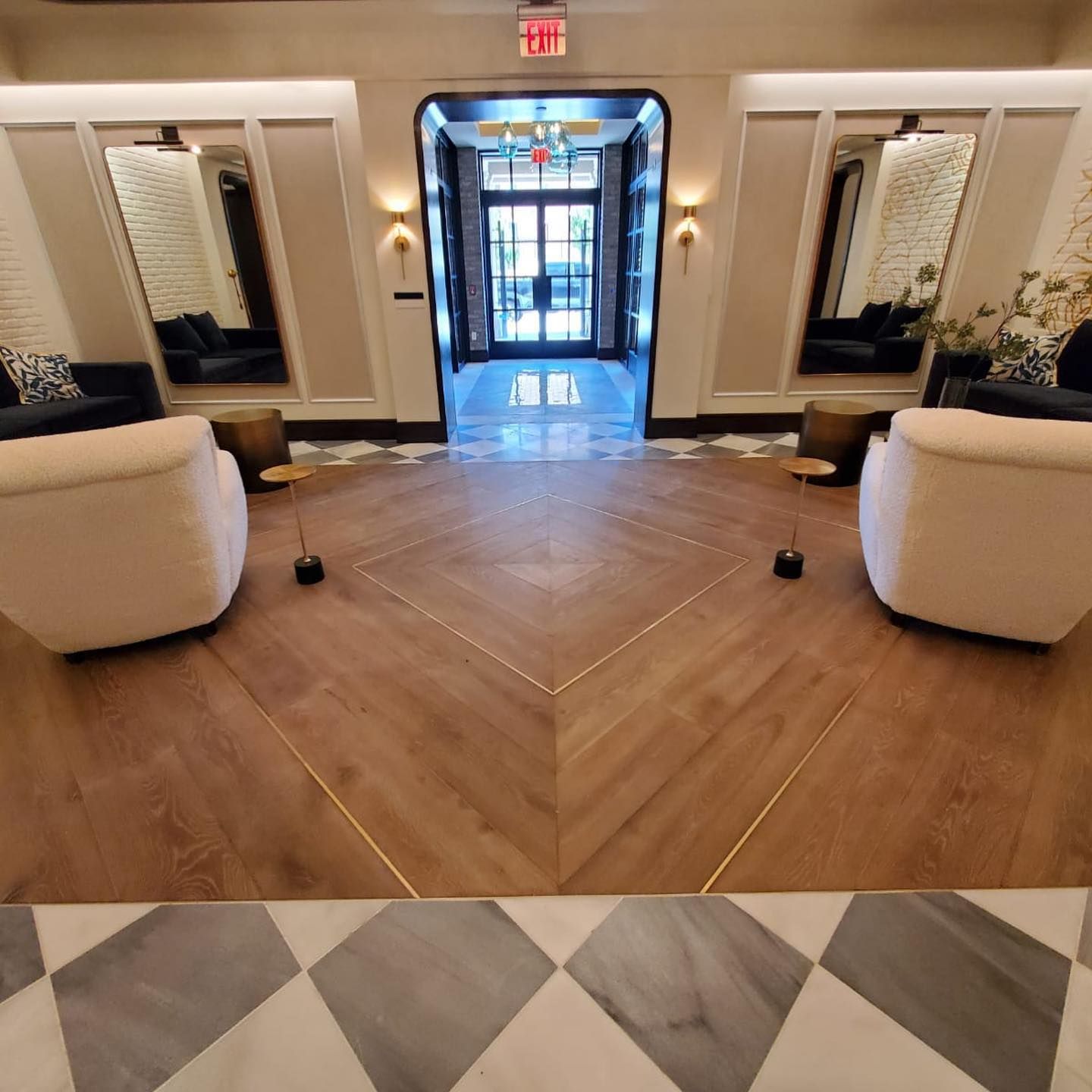 Lobby with wood floor, white chairs, tall mirrors, and a view of an exterior door.