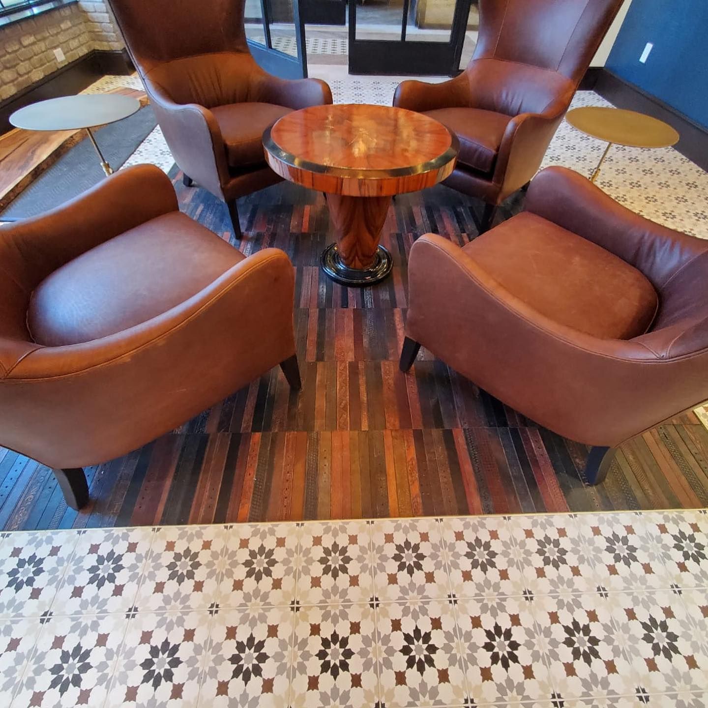 Four brown leather chairs around a decorative wooden table on a patterned floor.