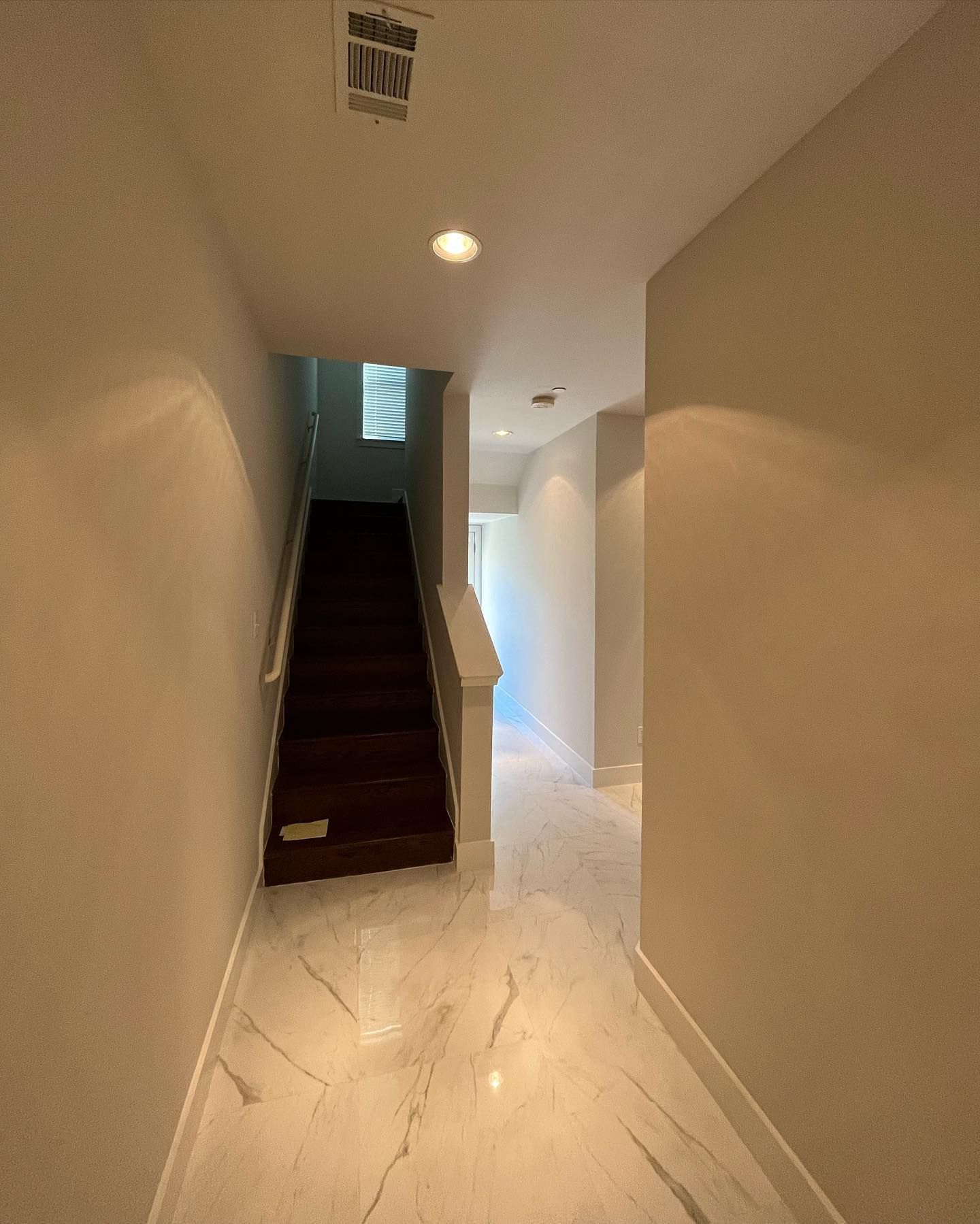 Hallway with marble floor, leading to stairs and an upper level with window.