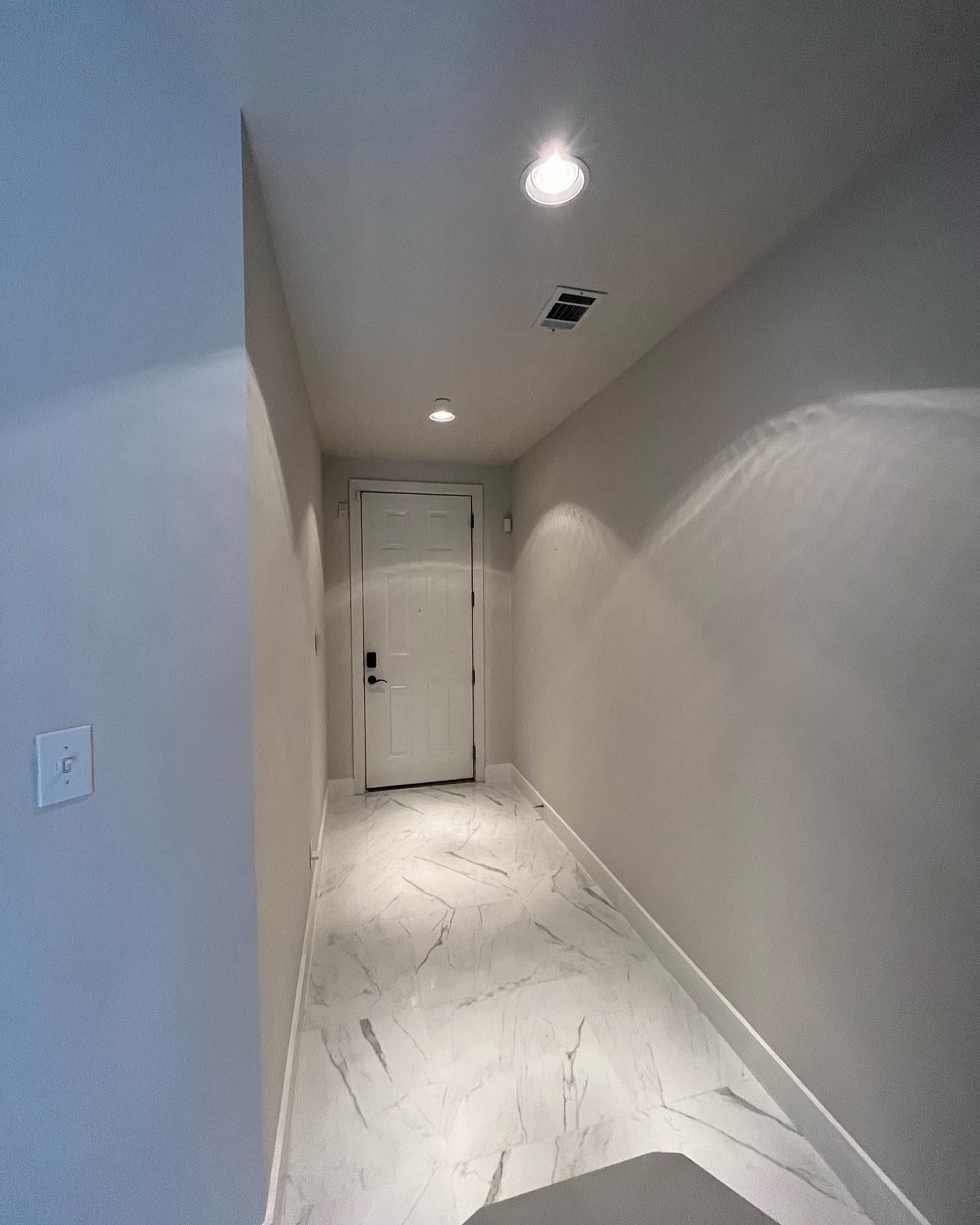 Hallway with white walls, marble floor, and door at the end. Two ceiling lights illuminate the space.
