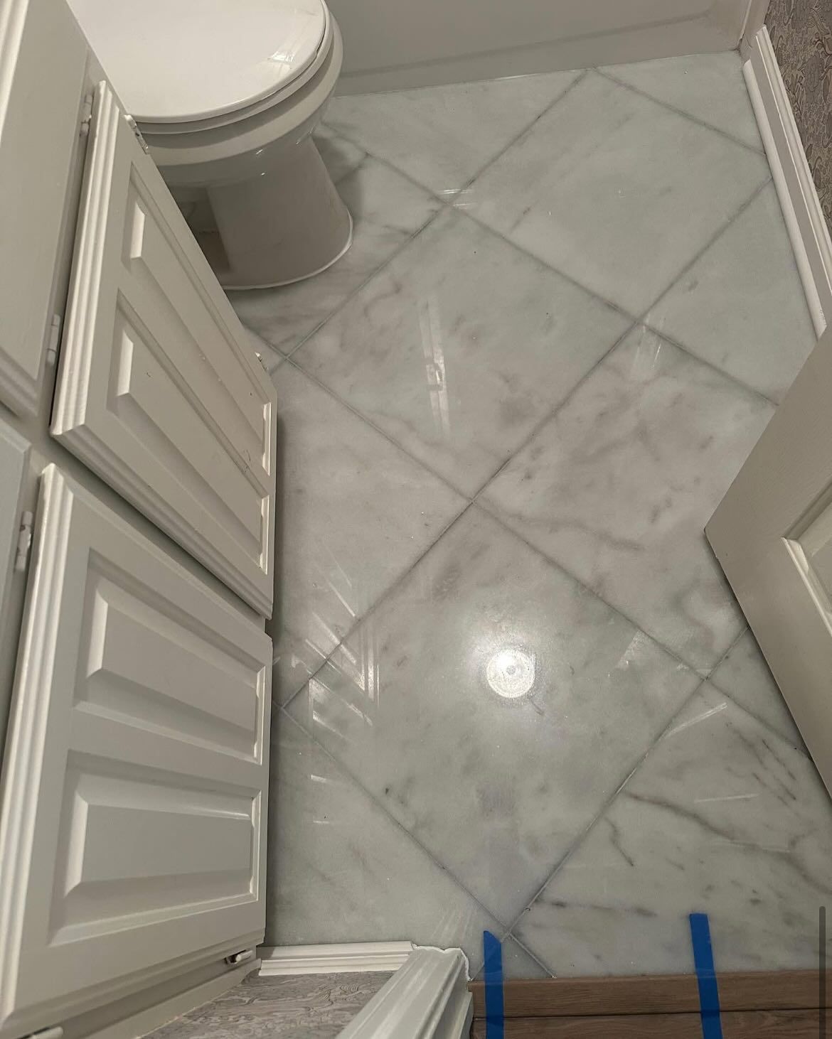 Bathroom floor with diagonally laid gray marble tiles, toilet, and white cabinets.