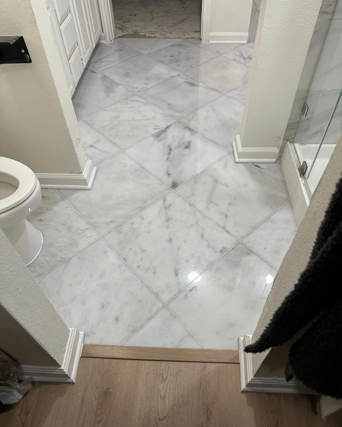 White marble tile floor in a bathroom, with a toilet on the left and a shower on the right.