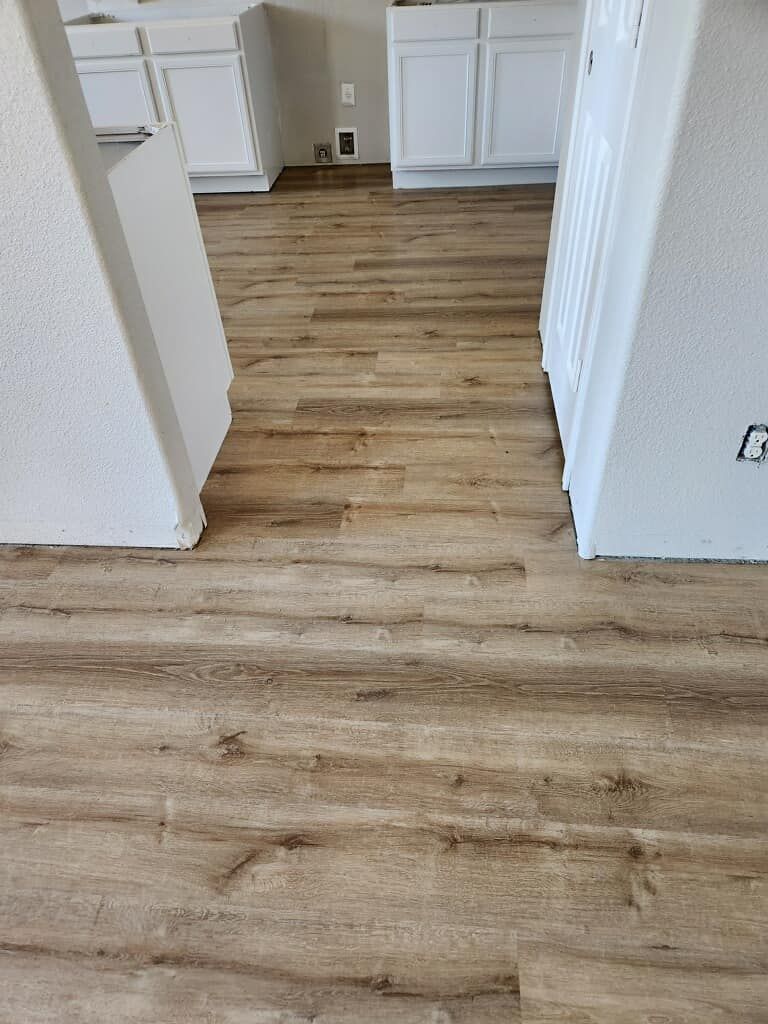 Wooden floor hallway with a dark wooden door, staircase, and chandelier in the background.