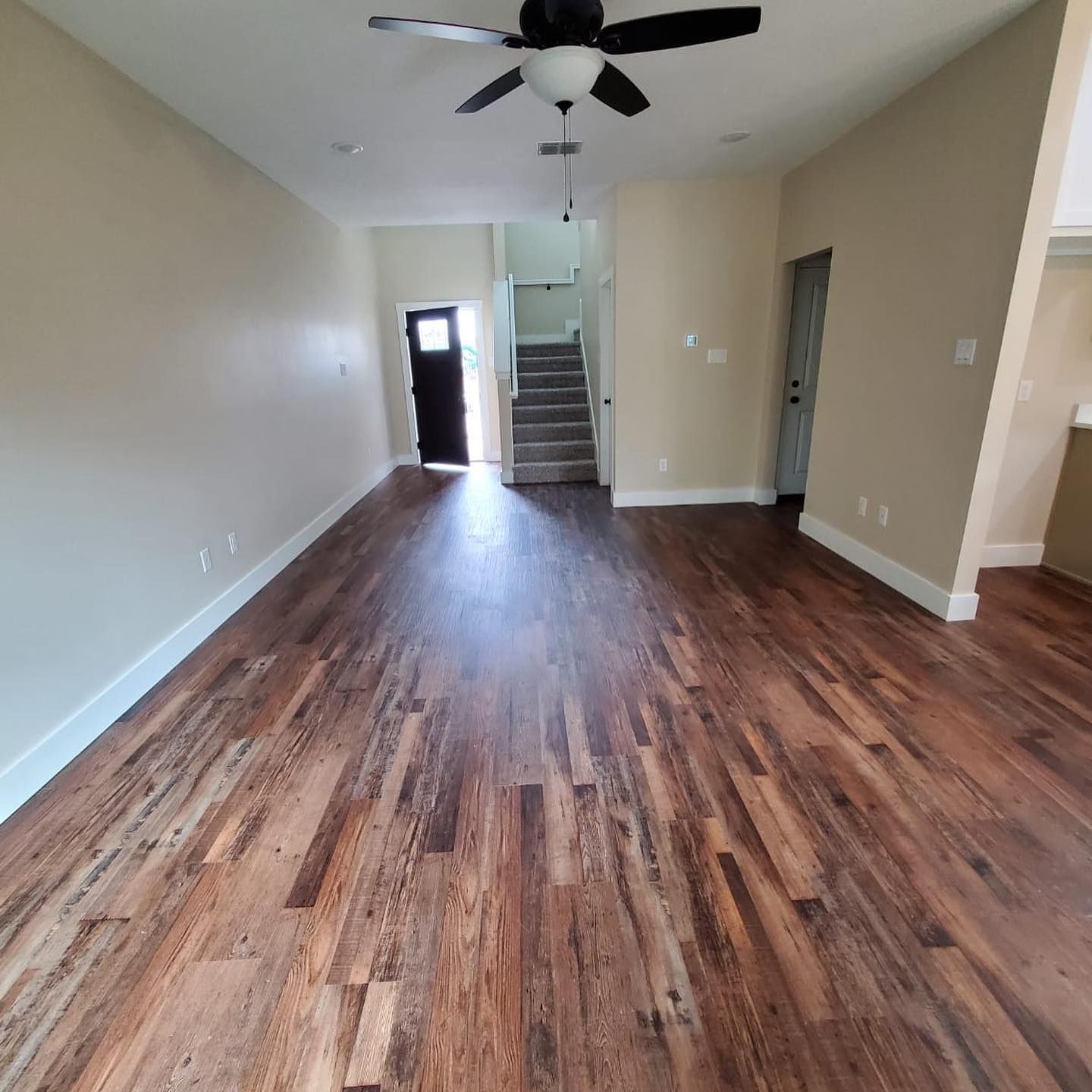 Empty living room with wood floors, beige walls, and a staircase.