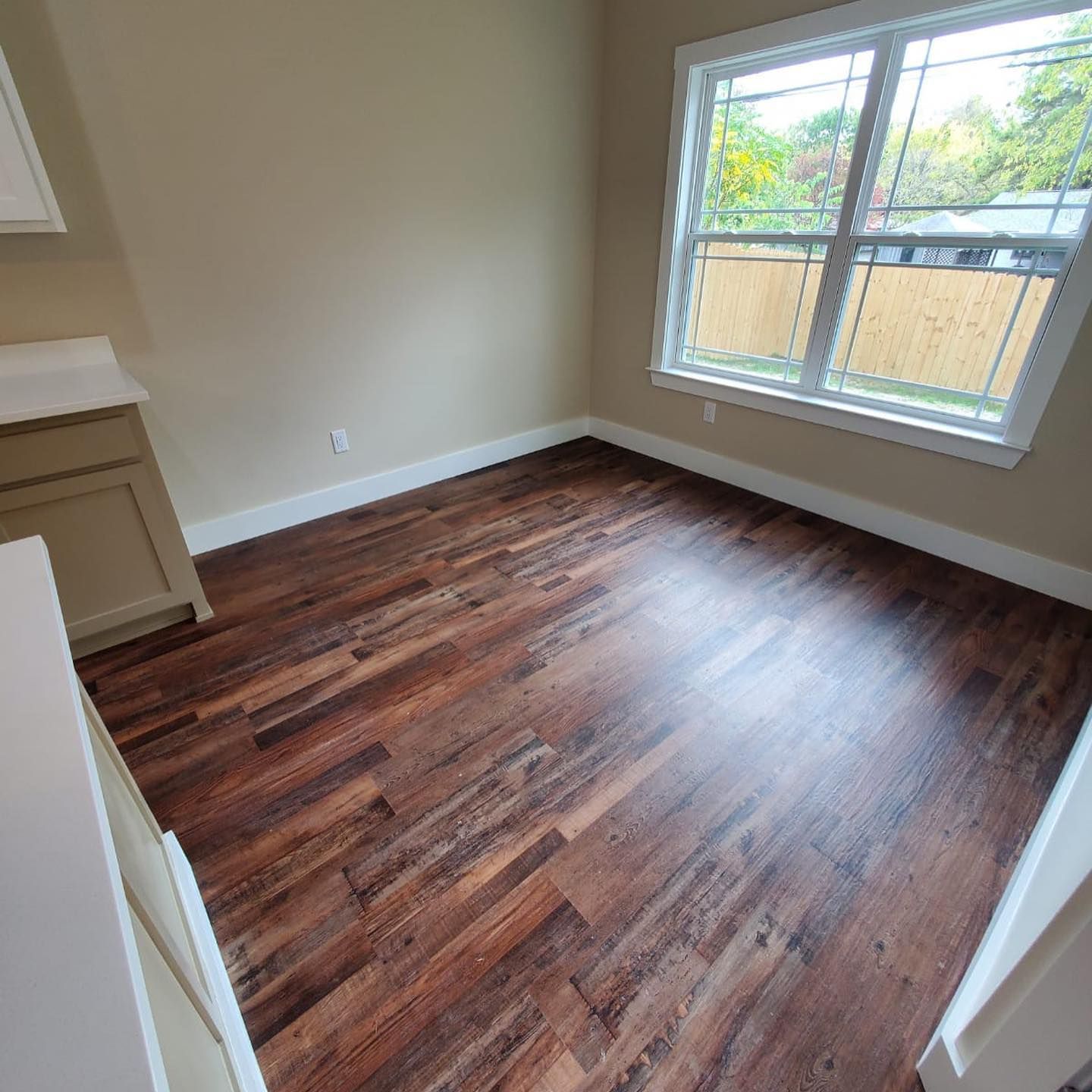 Empty room with hardwood-style floor, beige walls, window, and cabinetry; a bright space.