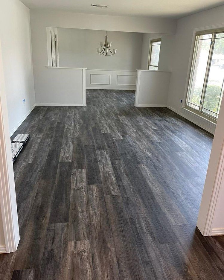 Gray wood-look flooring in a living room, white walls, and an open dining room with a chandelier.
