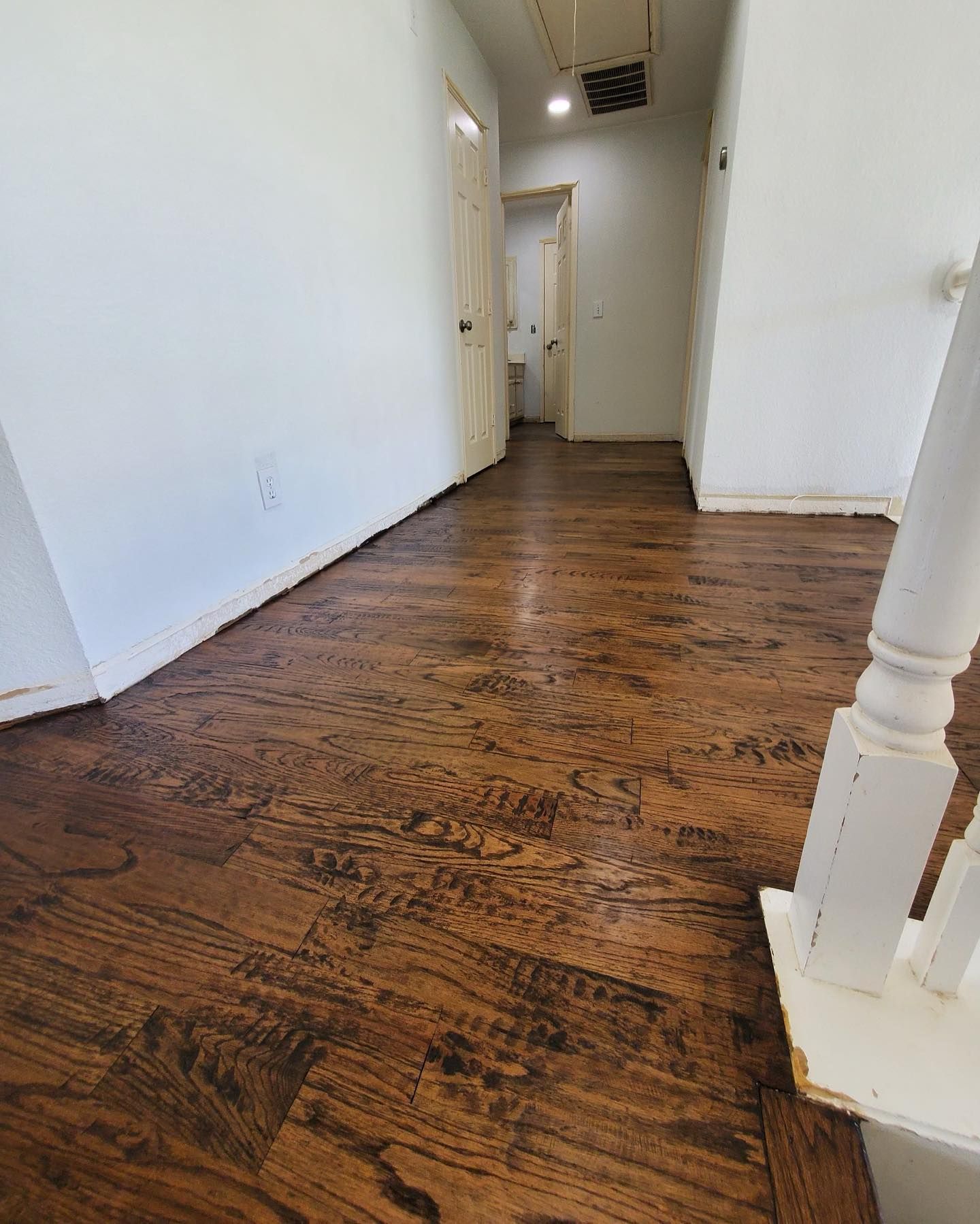 Hallway with wood floors, white walls, and doors. Wooden handrail on right.