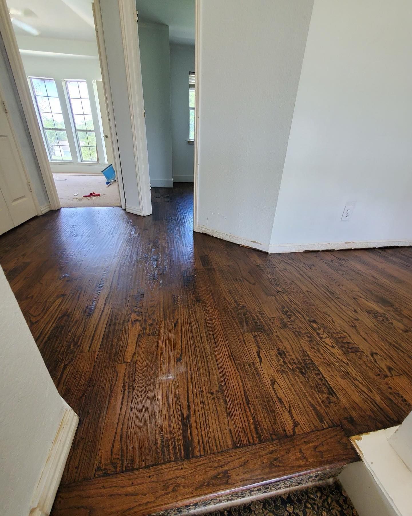Dark stained hardwood floors in a home; entryway with doors and a small step; light-colored walls.