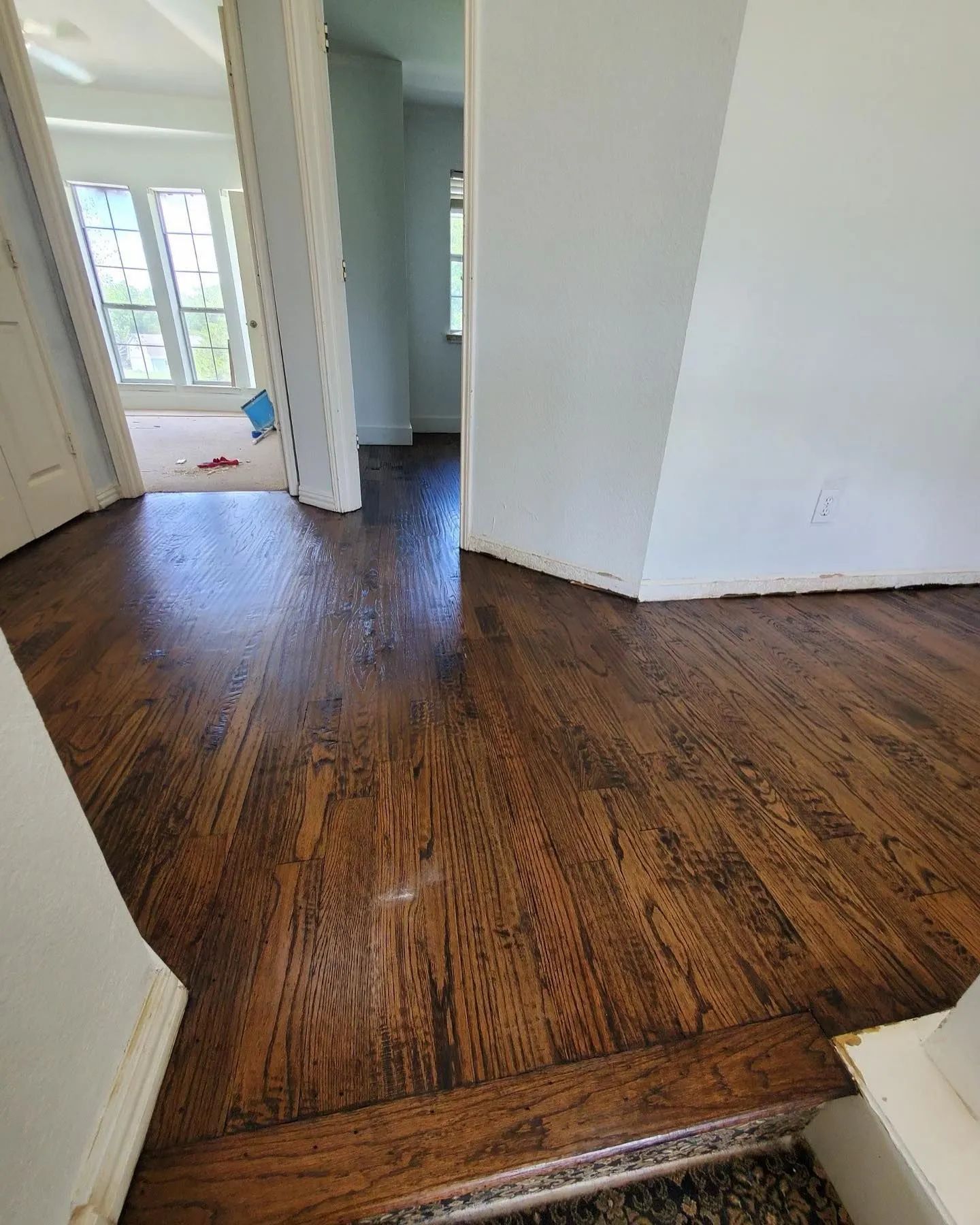 Dark wood floors with a shiny finish in a hallway, leading to other rooms with white walls.