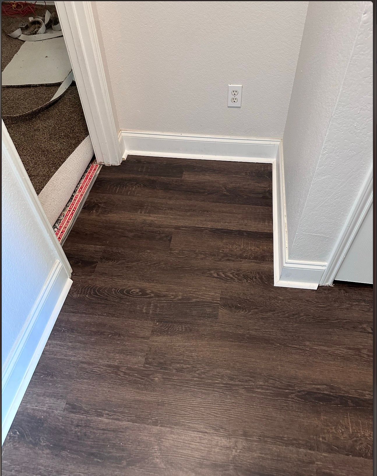 Dark wood-look flooring in a doorway, with white trim and a wall outlet.