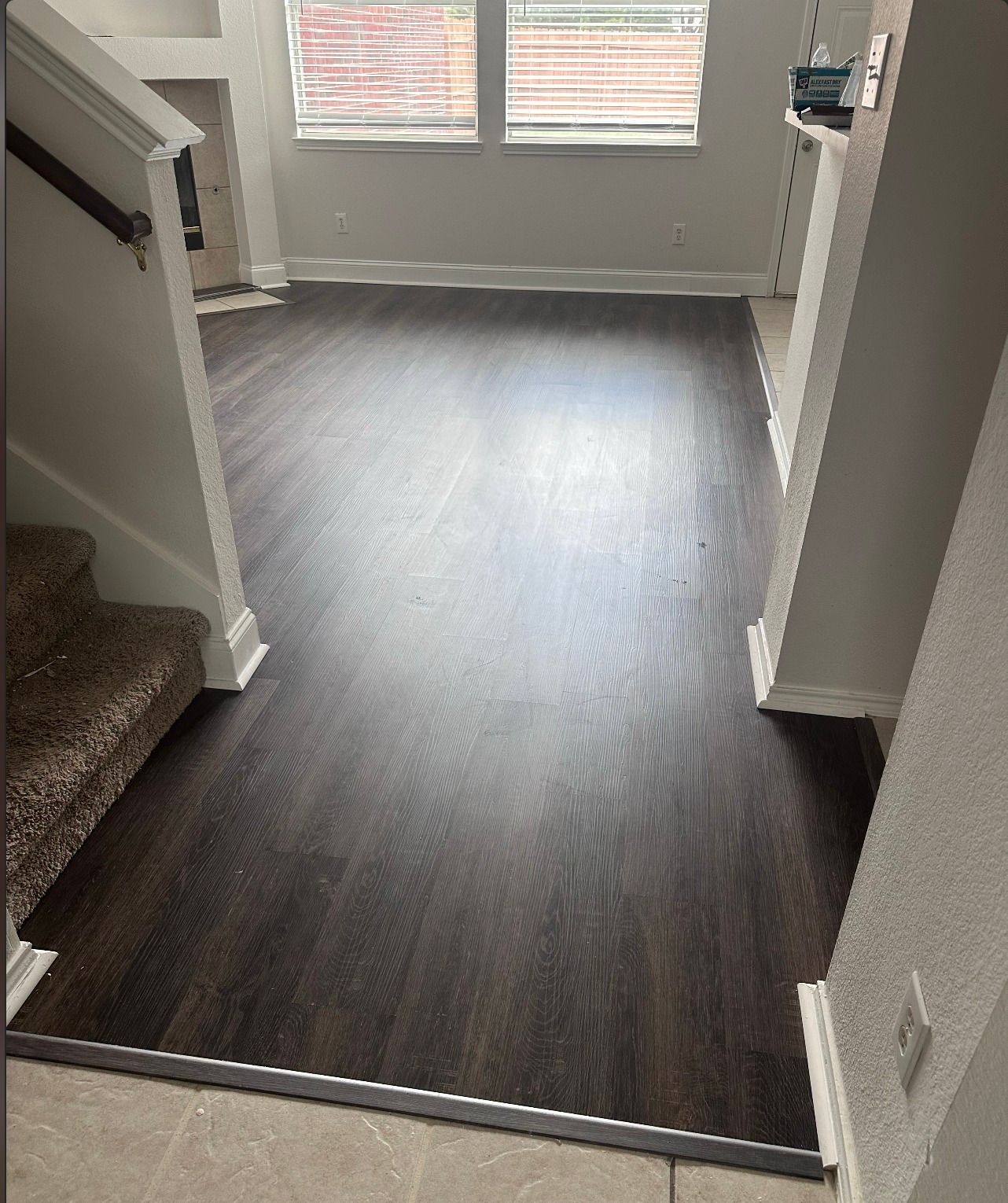 Dark wood-look flooring leads from stairs to a bright room with windows.