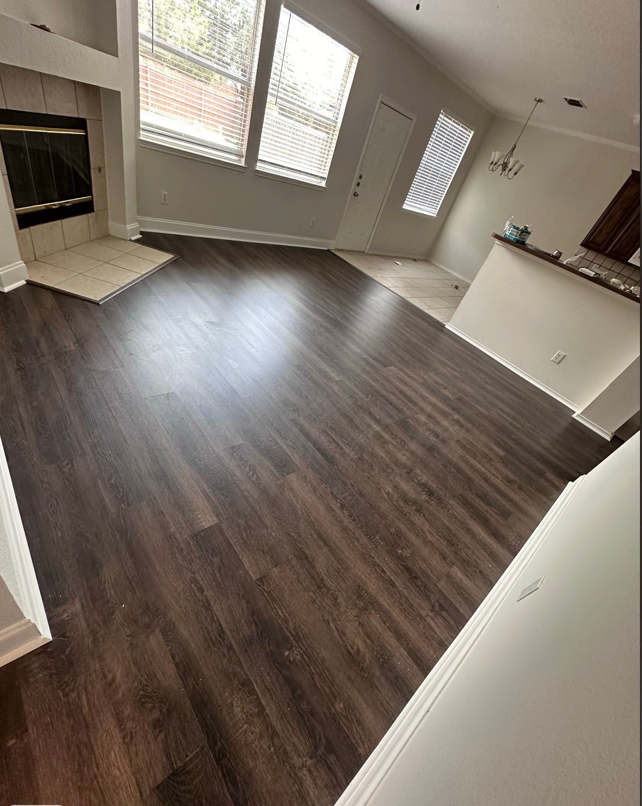 Living room with dark wood-look flooring, fireplace, large windows, and a light-colored wall.