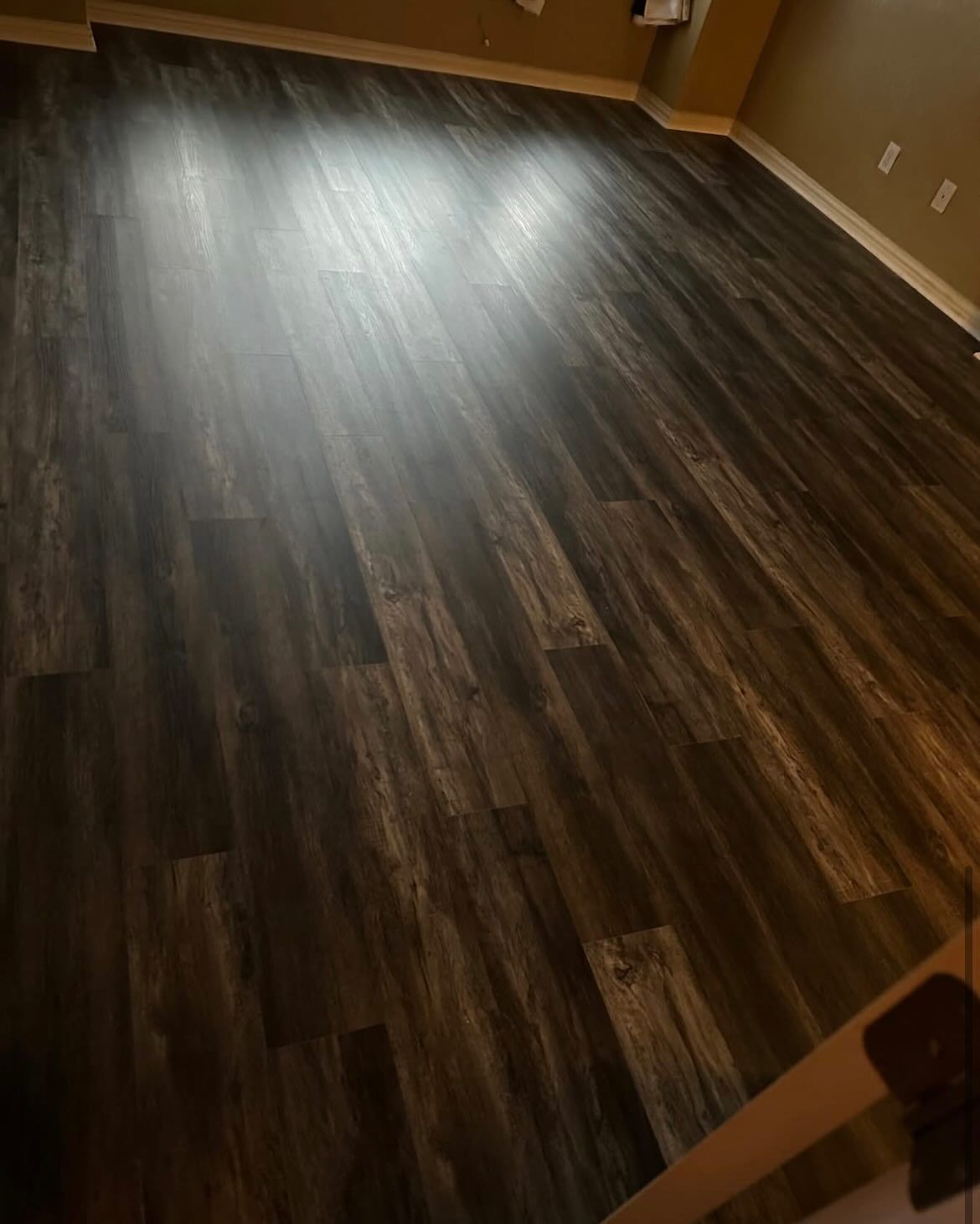 Dark brown wood-look flooring in a room; light reflects off the surface.