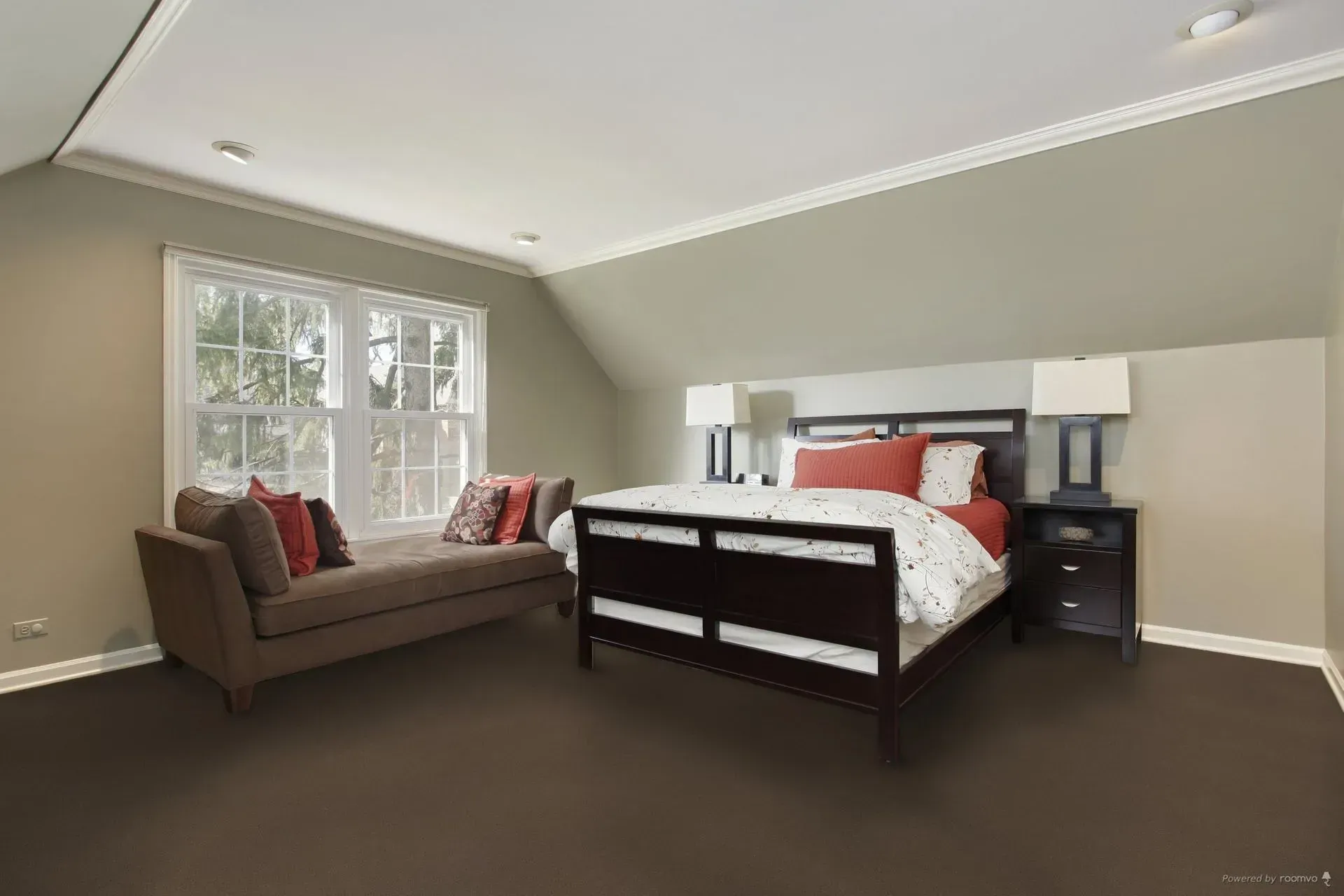 Bedroom with bed, window seat, nightstand, and neutral-colored walls and brown carpet.