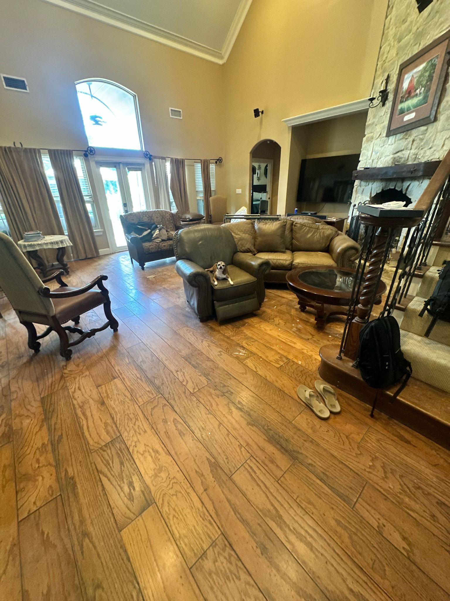 Spacious living room with hardwood floors, leather sofas, a fireplace, and large windows.
