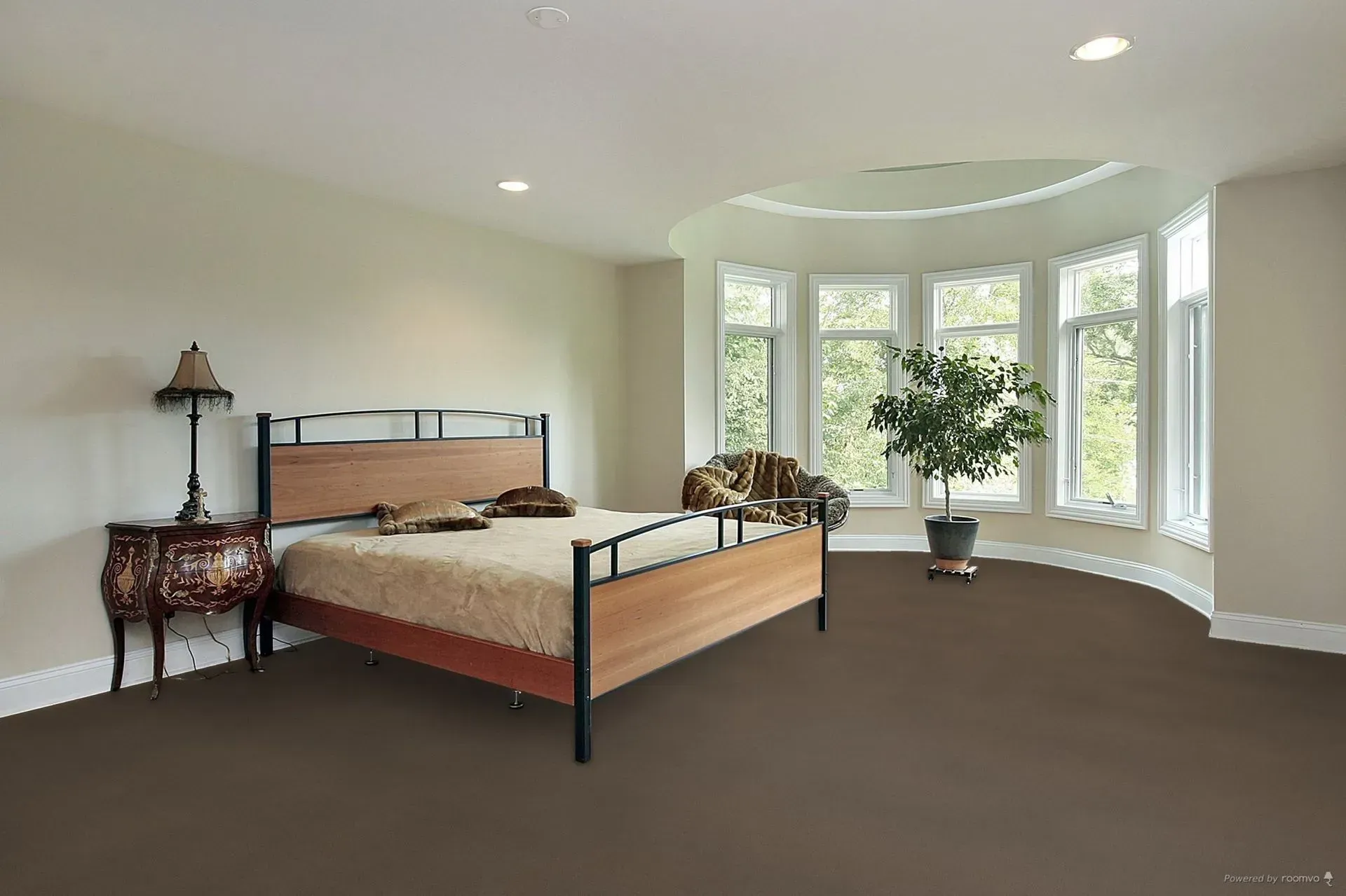 Bedroom with bed, nightstand, chair, large windows, and indoor tree; brown carpet.