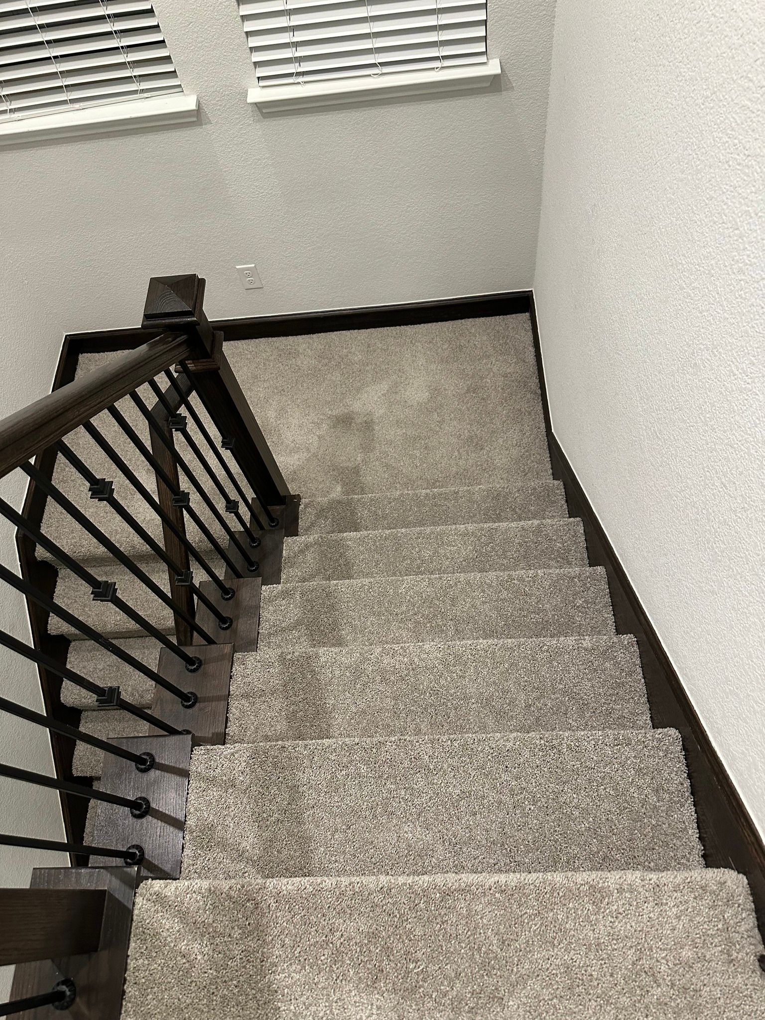Staircase with gray carpet and dark wood banister, descending from top to bottom.