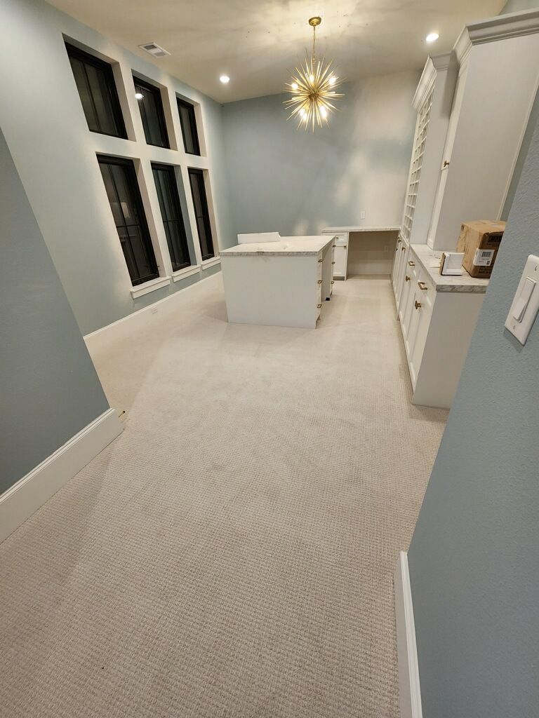 Bright home office with light gray walls, white built-ins, a desk, and patterned carpet.