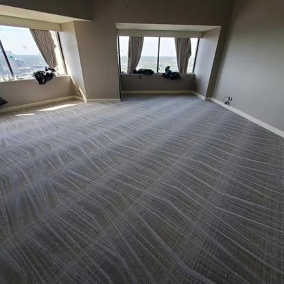 Empty room with gray patterned carpet, multiple windows with curtains.