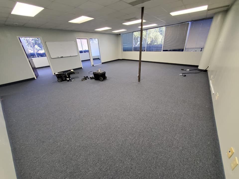 Empty office space with blue carpet, windows, and a center pole.