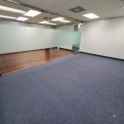 Empty office space with blue carpet, glass walls, and wood flooring.