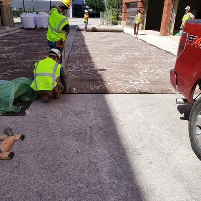 Construction workers installing pavement with red pickup truck parked nearby.