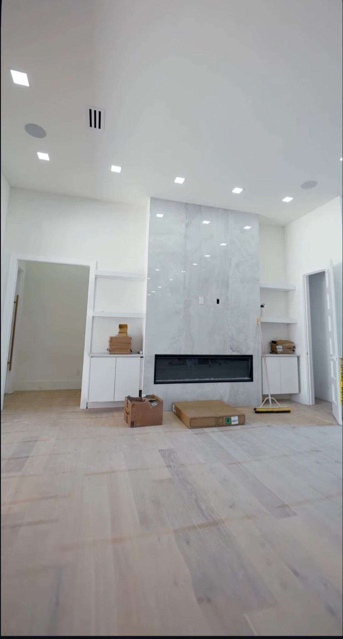 Empty room with fireplace, built-in shelves, and light wood floors; under construction, bright lighting.
