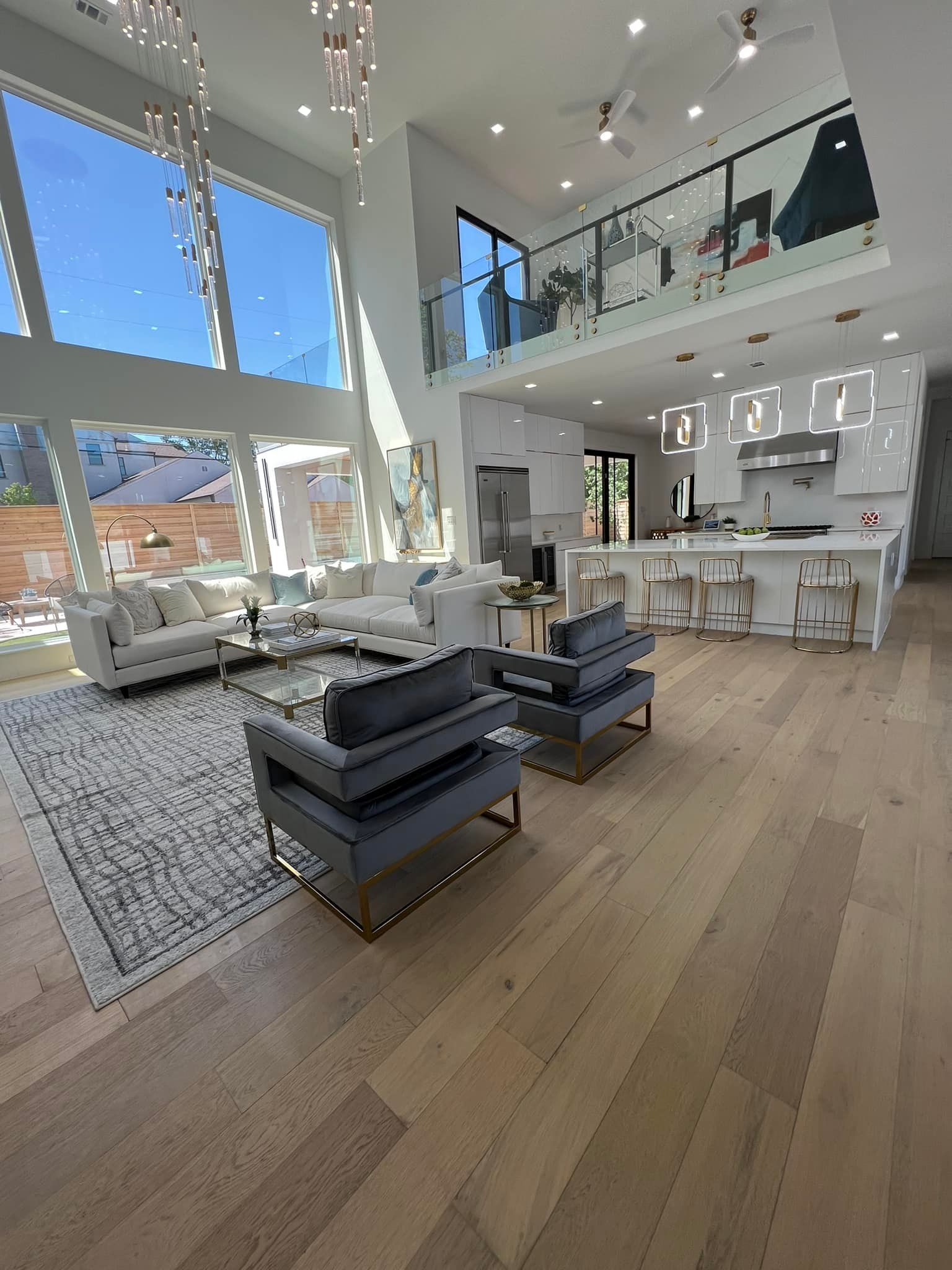 Modern living room with large windows, light wood floors, and blue-gray armchairs.