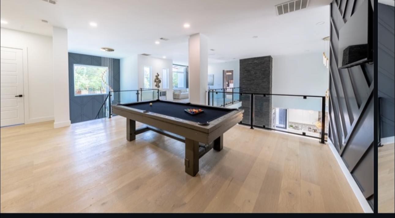 Spacious game room with a pool table, glass railings, and light wood flooring.