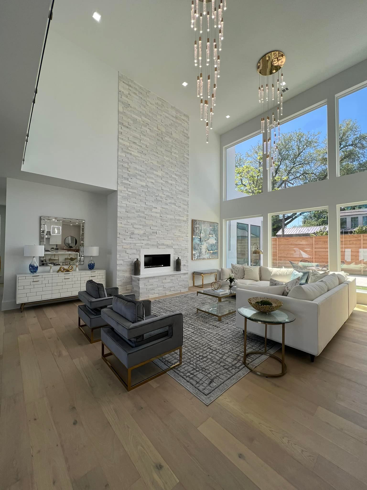 Modern living room with fireplace, large windows, white walls, and hardwood floors.